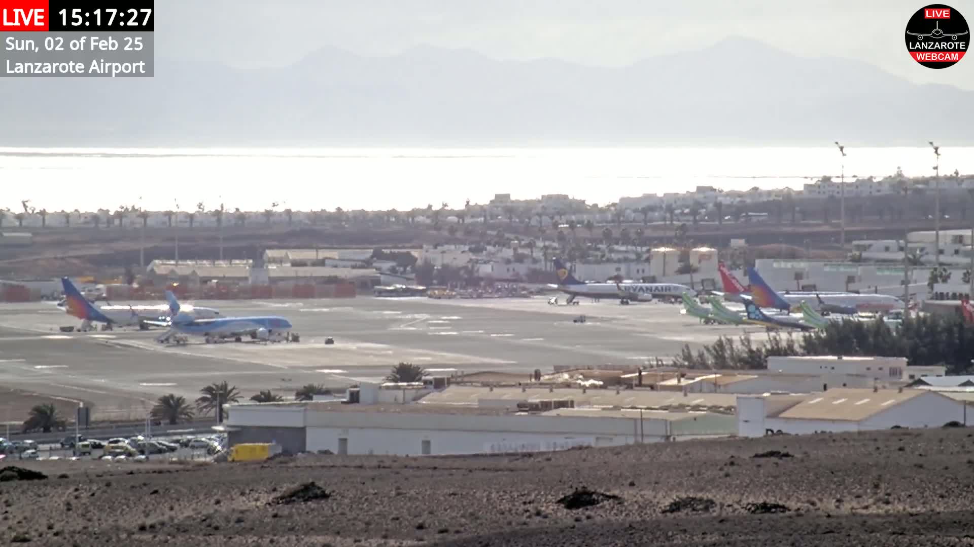 Several airplanes are parked on a tarmac at an airport near a body of water under hazy daylight conditions.