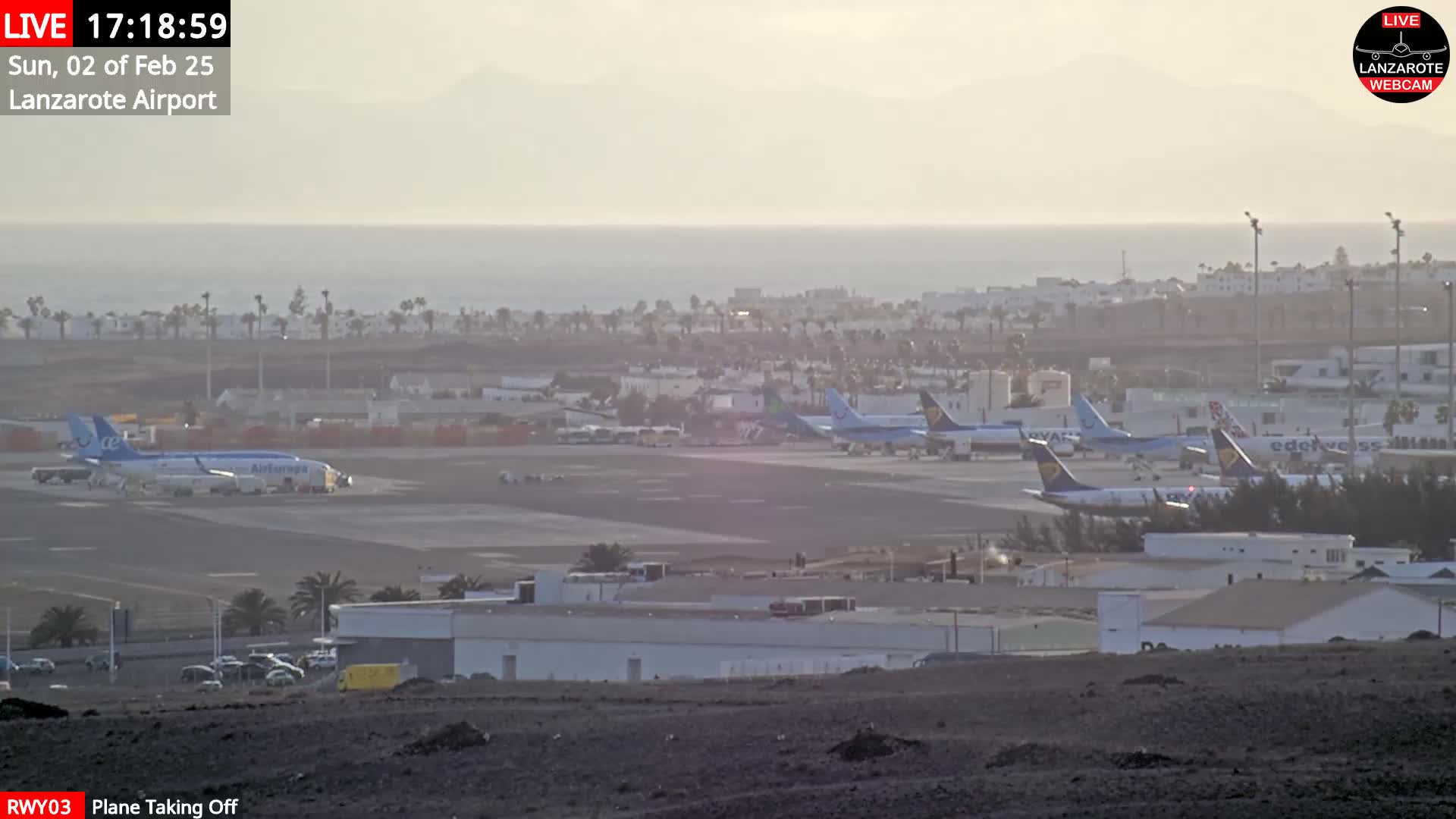 Several airplanes are parked on a hazy airport tarmac near a body of water under a light, hazy sky.