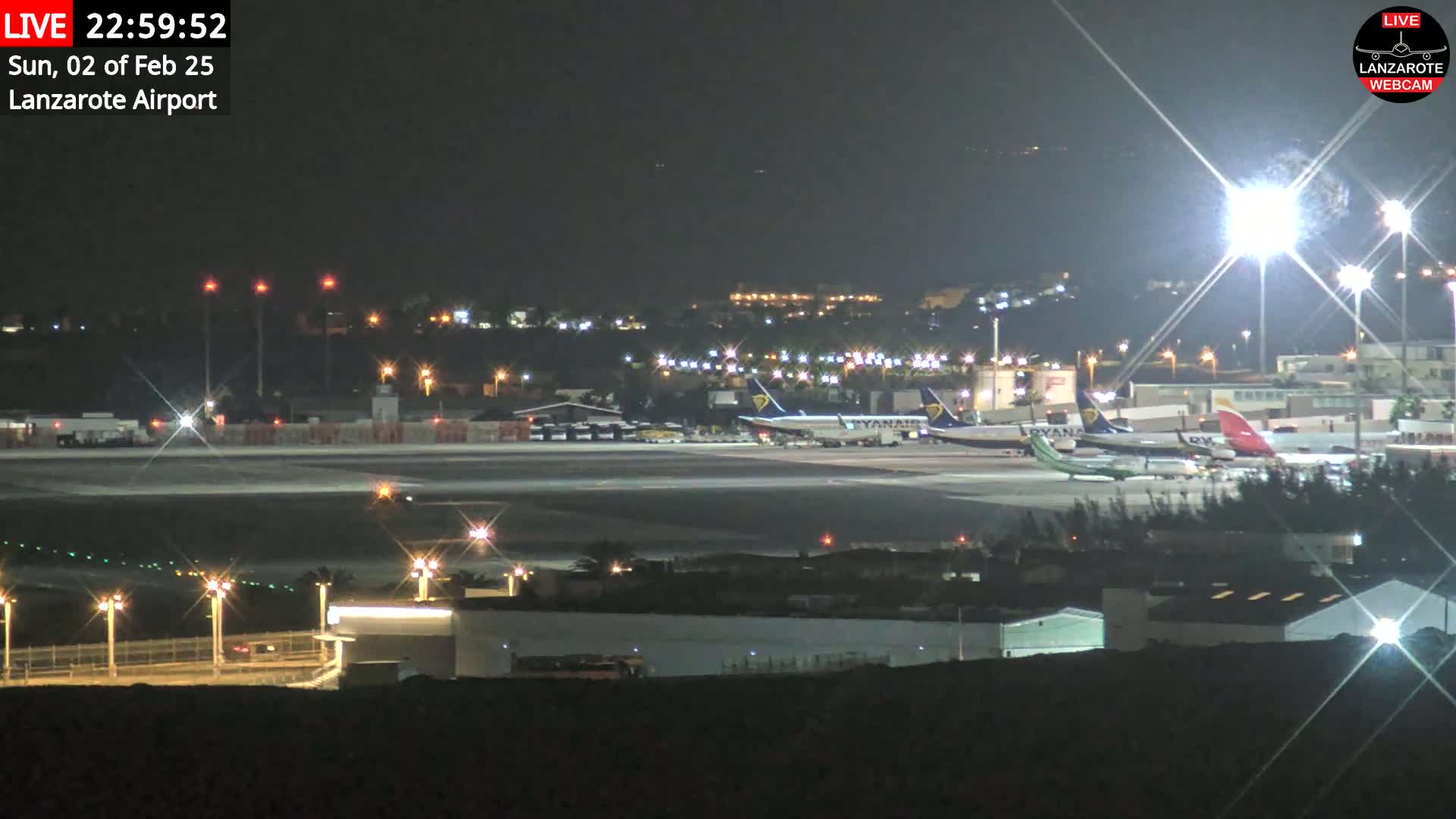 A nighttime view of an airport tarmac with several airplanes parked, illuminated by bright lights under a clear, dark sky.