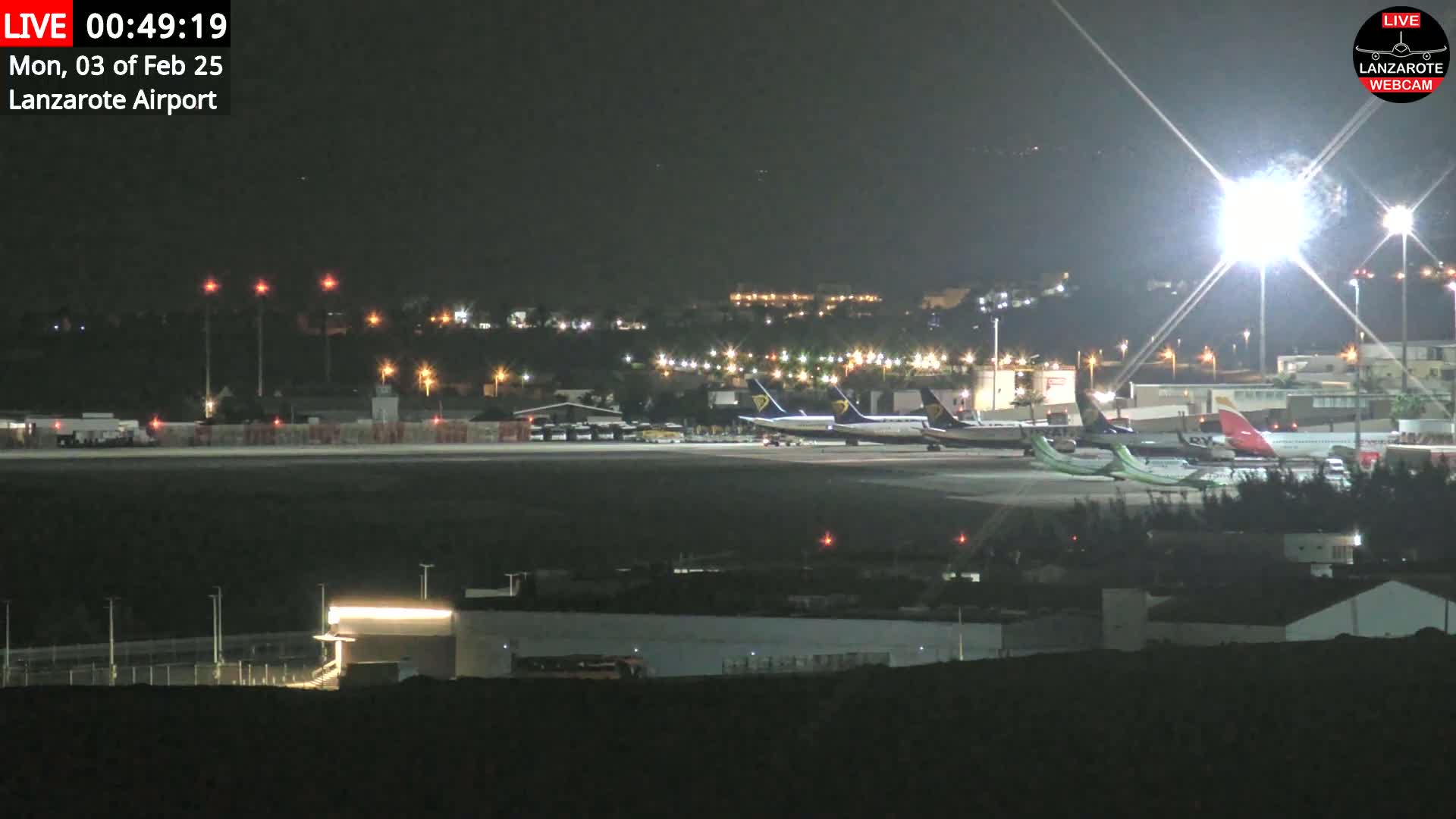 Several airplanes are parked on a tarmac at night under bright lights.