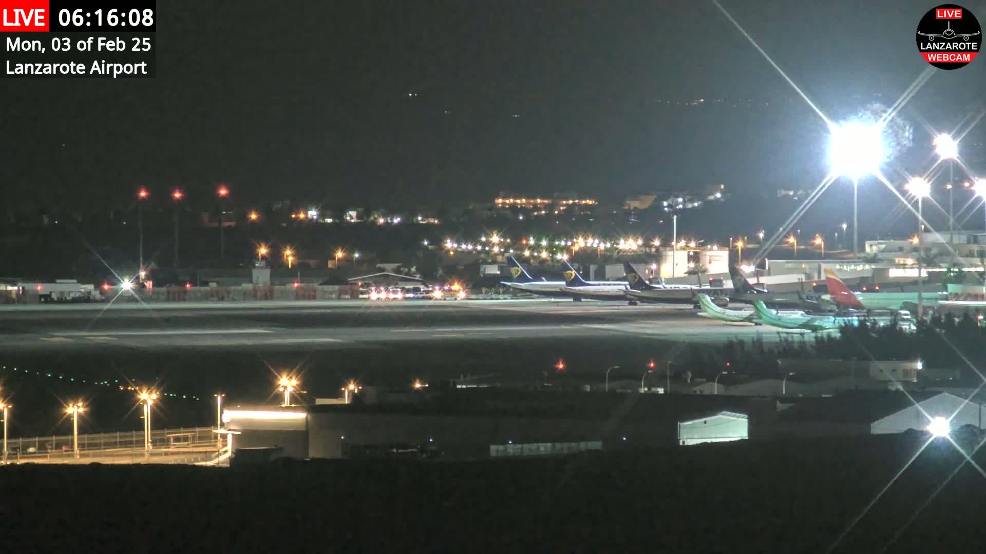 Several airplanes are parked on a brightly lit airport tarmac at night.