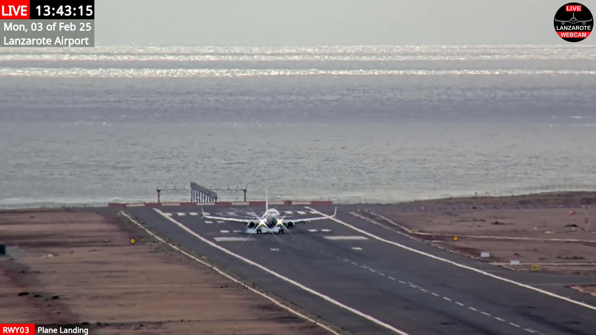 A white airplane is landing on a runway near a body of water under mostly clear skies.