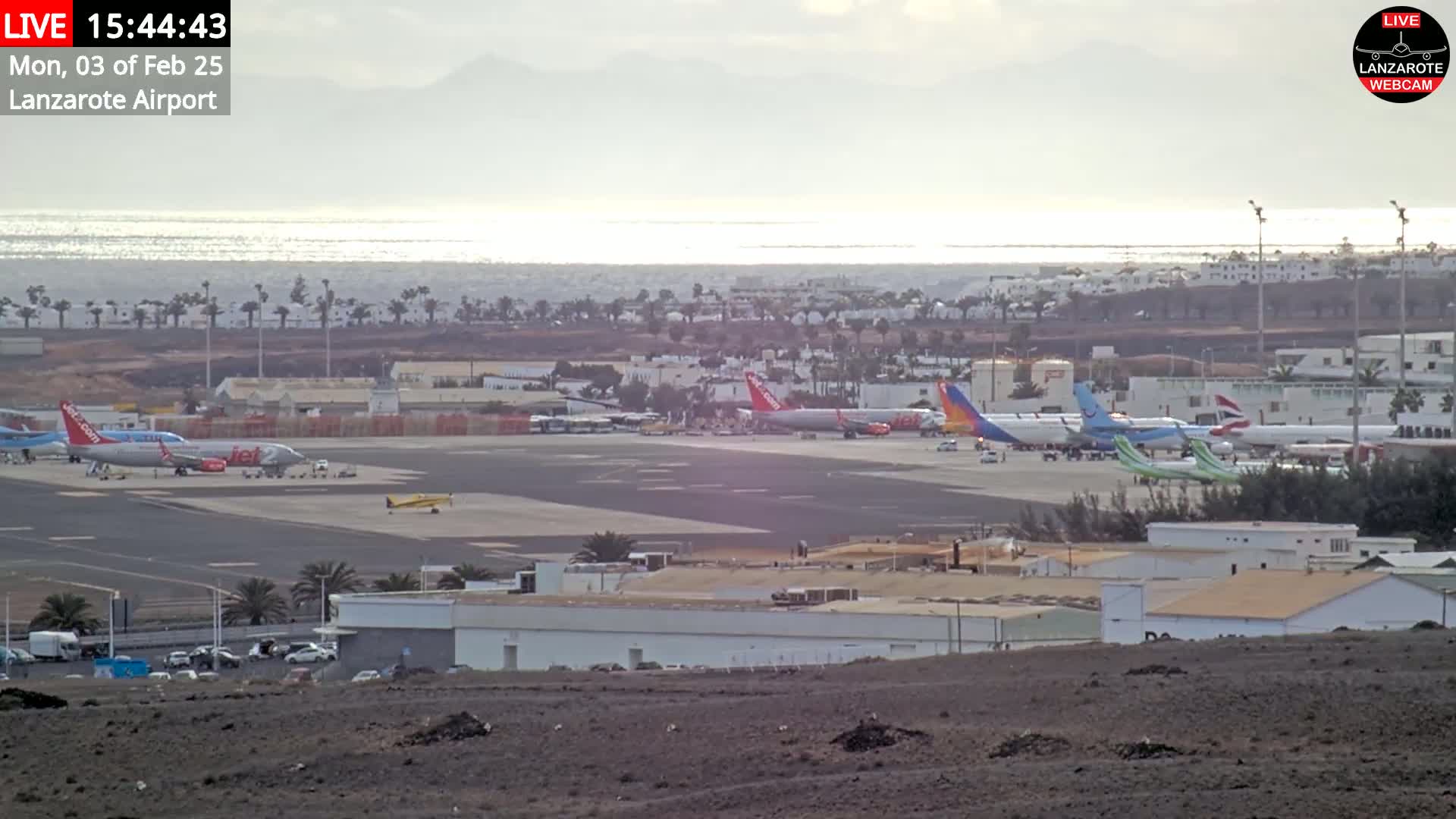 Several airplanes are parked on a tarmac at an airport near a body of water under a mostly cloudy sky.