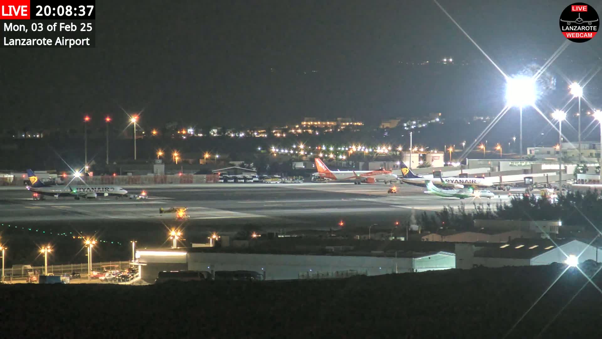 At night, several airplanes are parked on a brightly lit airport tarmac under clear skies.