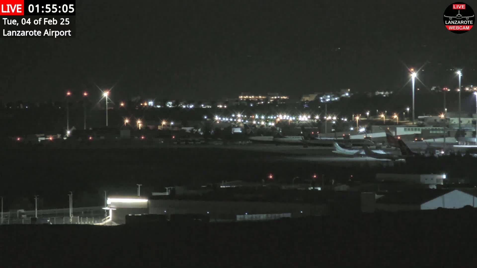 A nighttime view of an airport tarmac with several airplanes parked, surrounded by dimly lit buildings and lights.
