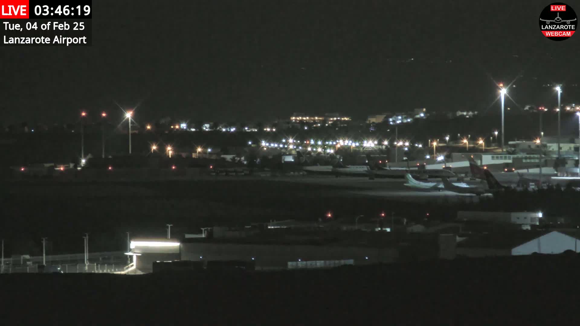 A nighttime view of an airport tarmac with several airplanes parked and illuminated by runway lights.