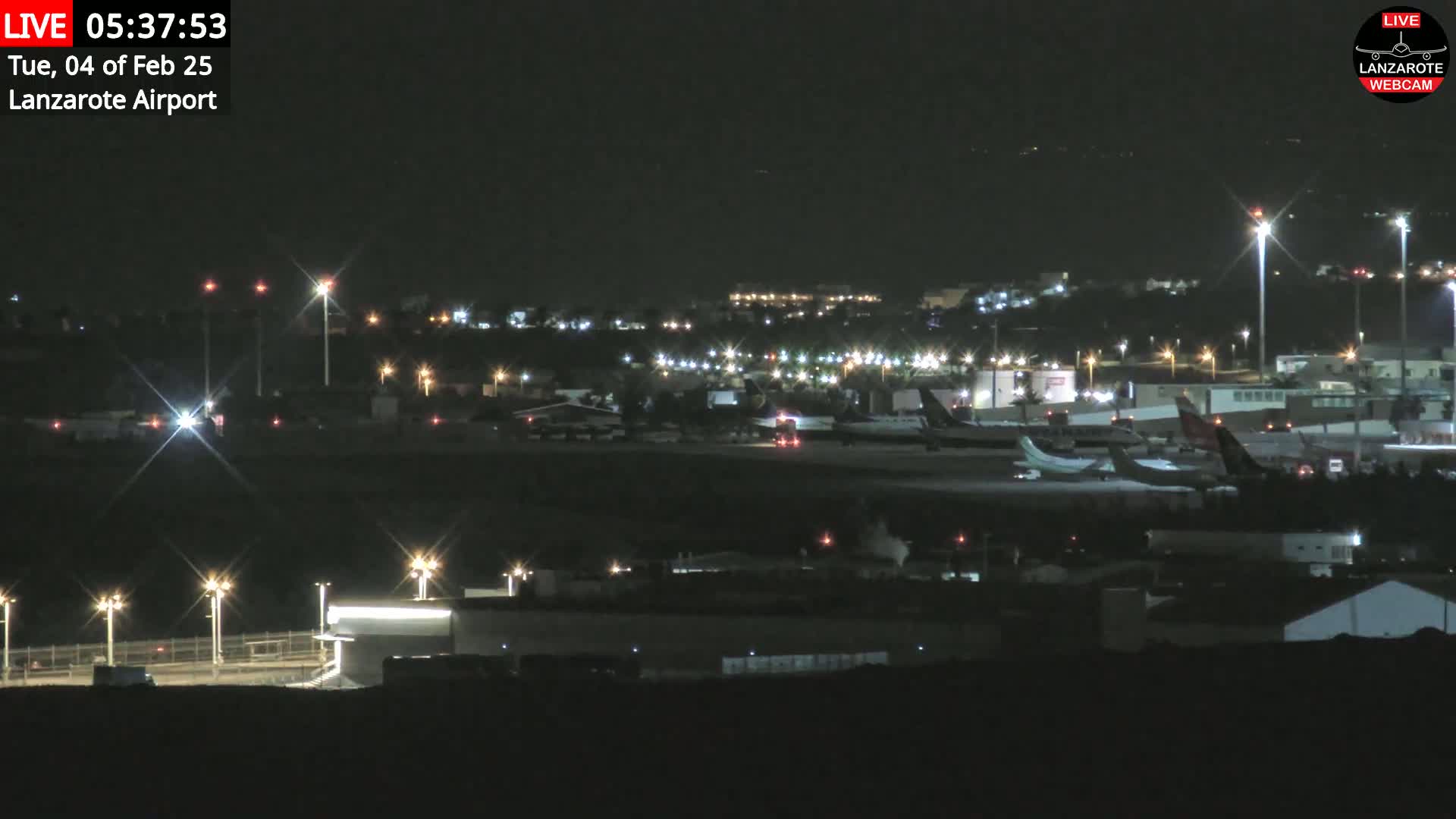 A nighttime view of an airport tarmac with several airplanes parked and illuminated by bright lights, under a clear, dark sky.