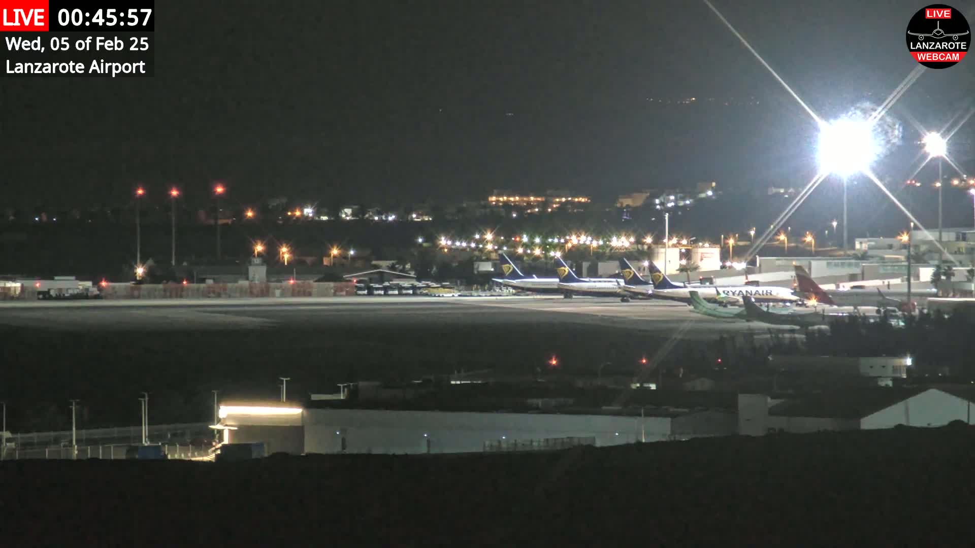 At night, several airplanes are parked on a brightly lit airport tarmac.
