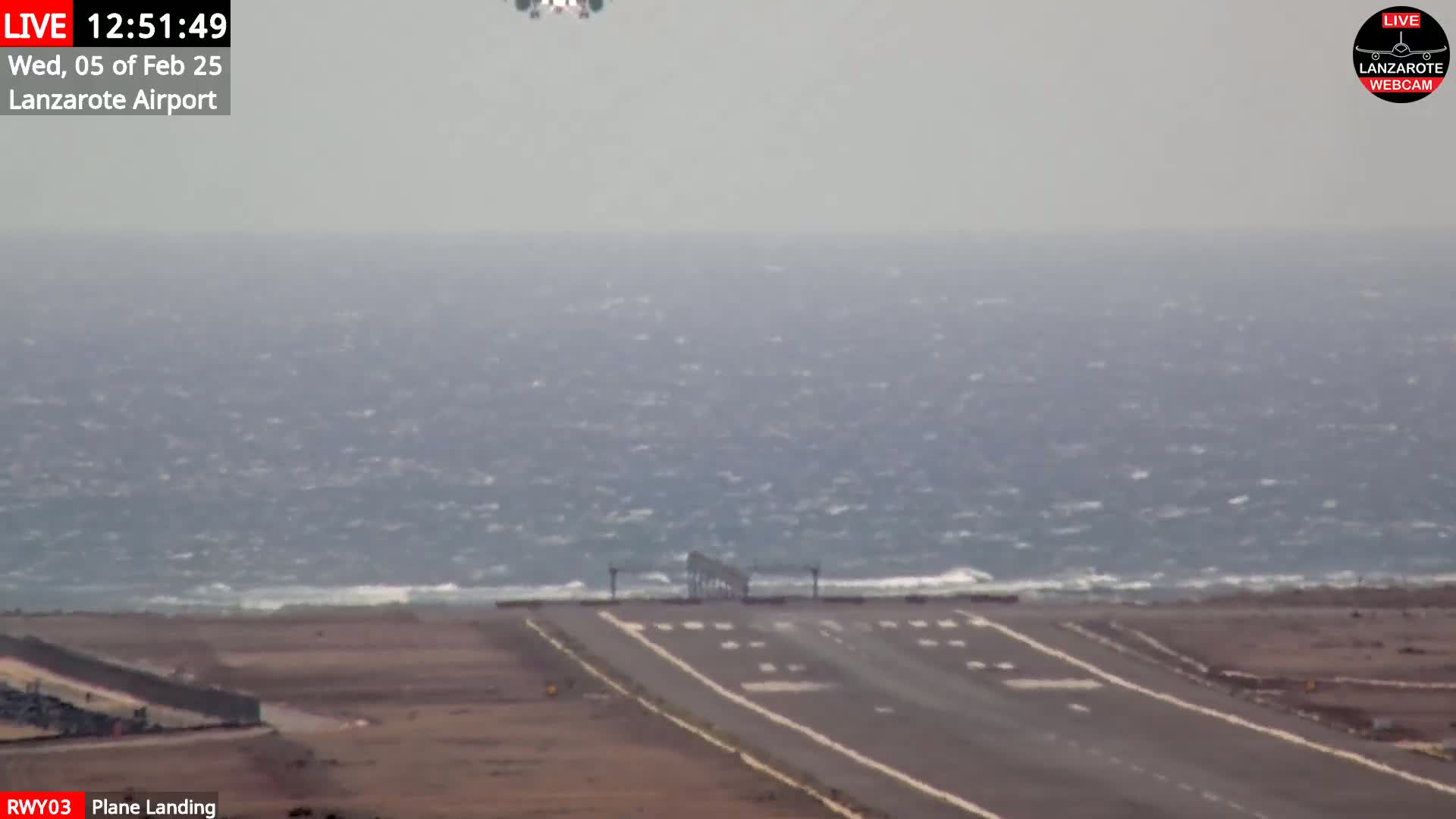 A runway at an airport adjacent to a choppy ocean under overcast skies.