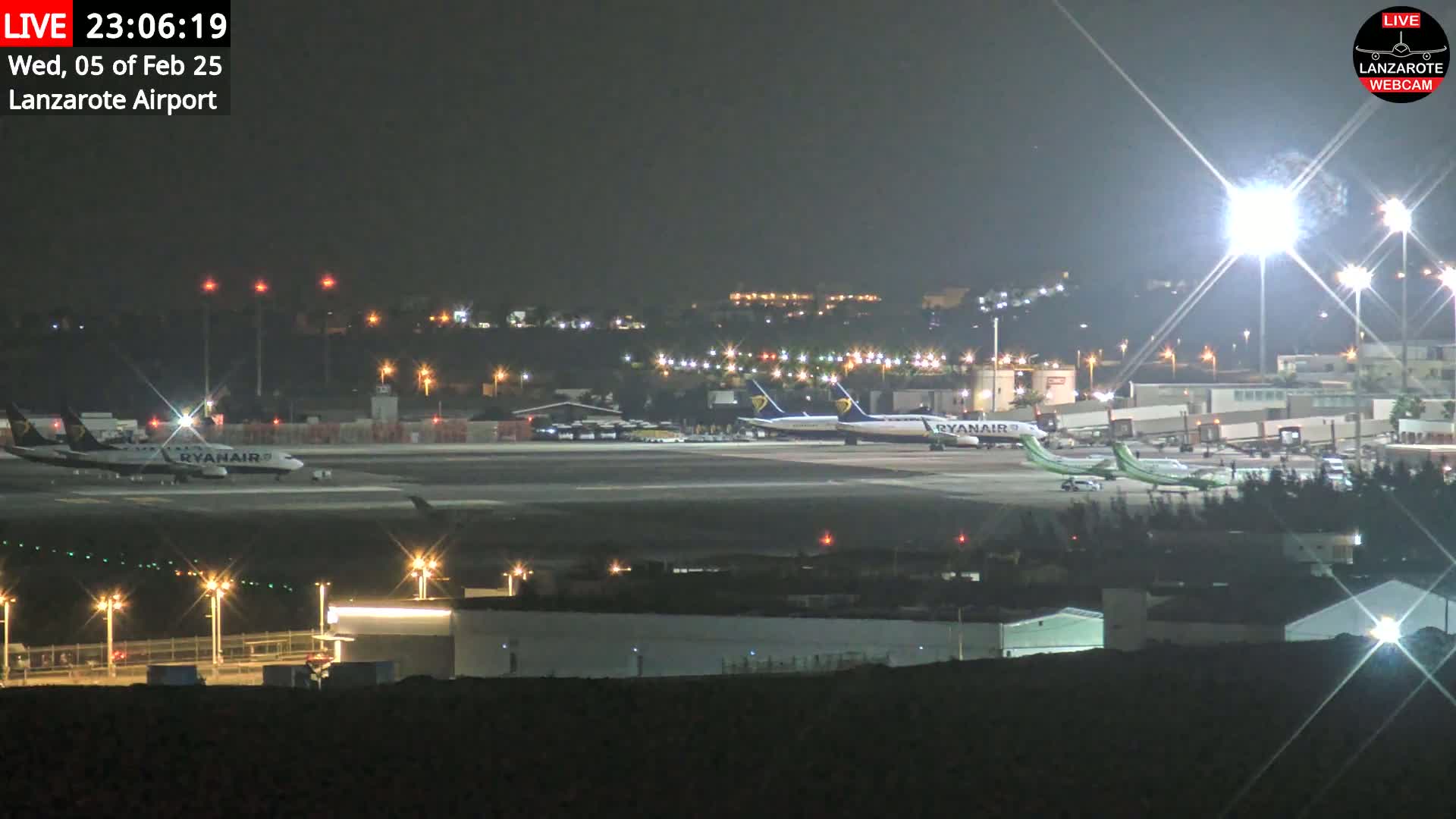 Several airplanes are parked on a brightly lit airport tarmac at night.