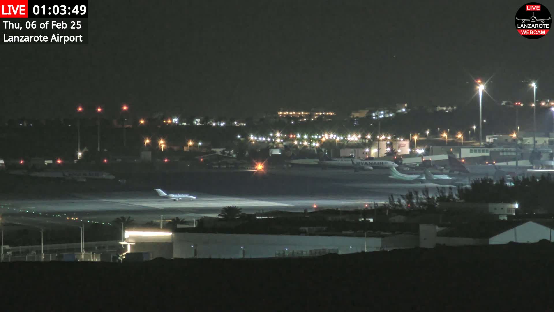 At night, a brightly lit airport tarmac shows several airplanes, including one that appears to be taxiing.