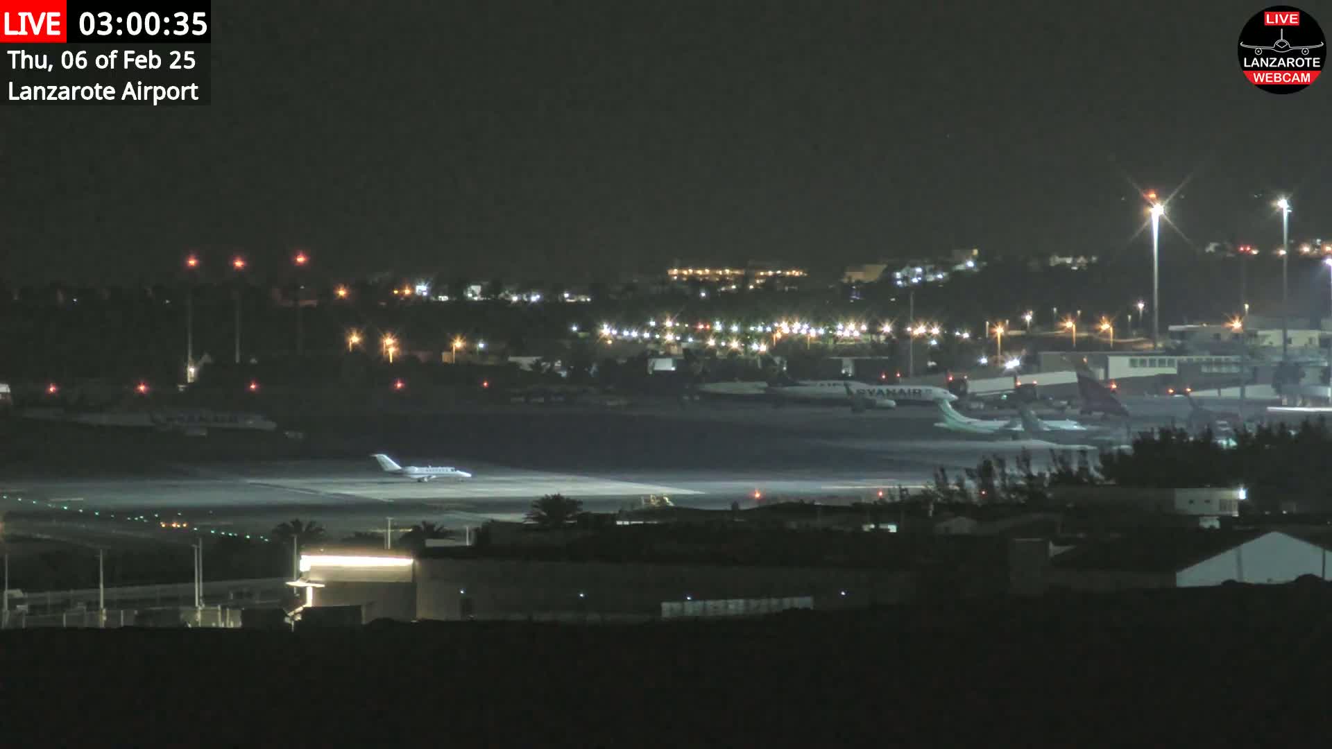 A nighttime view of an airport tarmac with several airplanes, including one taxiing on the runway, under clear skies.