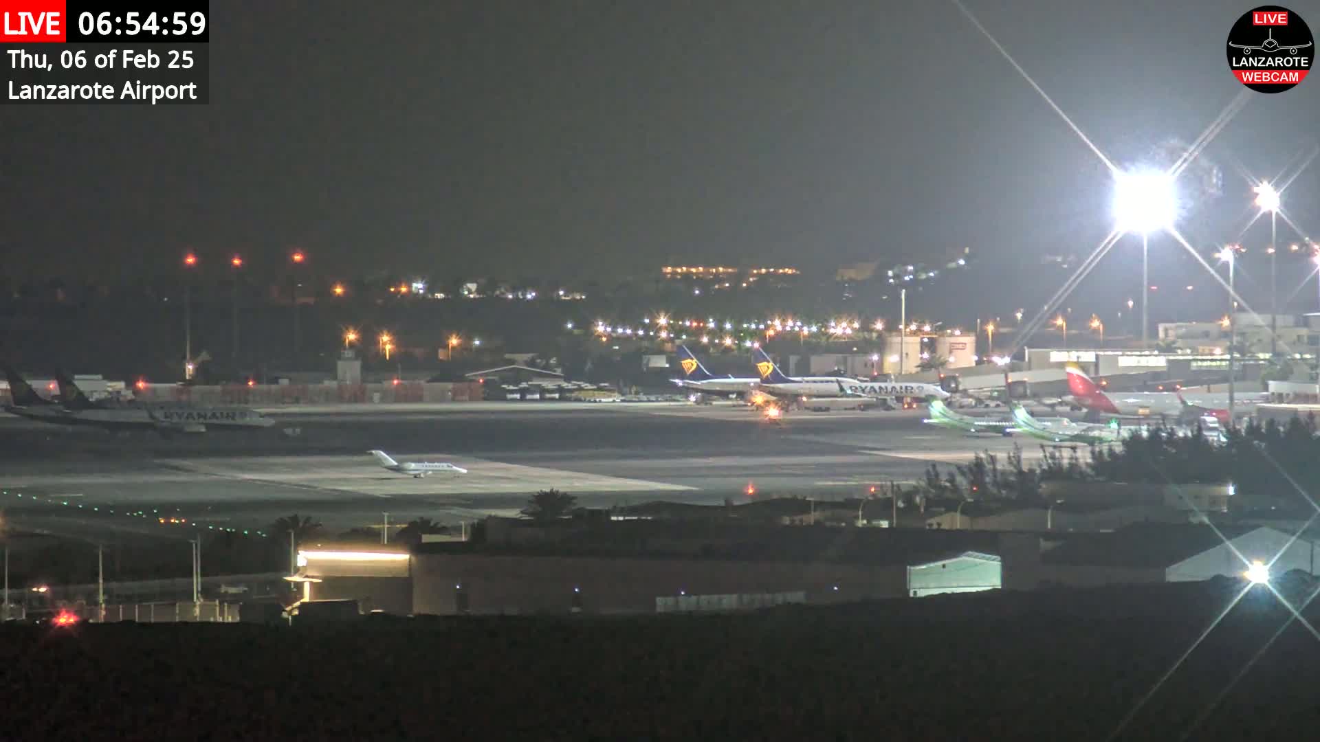 At night, several airplanes are parked on a brightly lit airport tarmac.