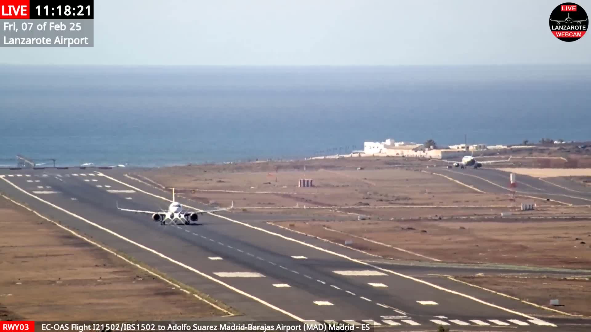 A commercial airplane taxis on a runway next to a calm ocean under a clear sky.