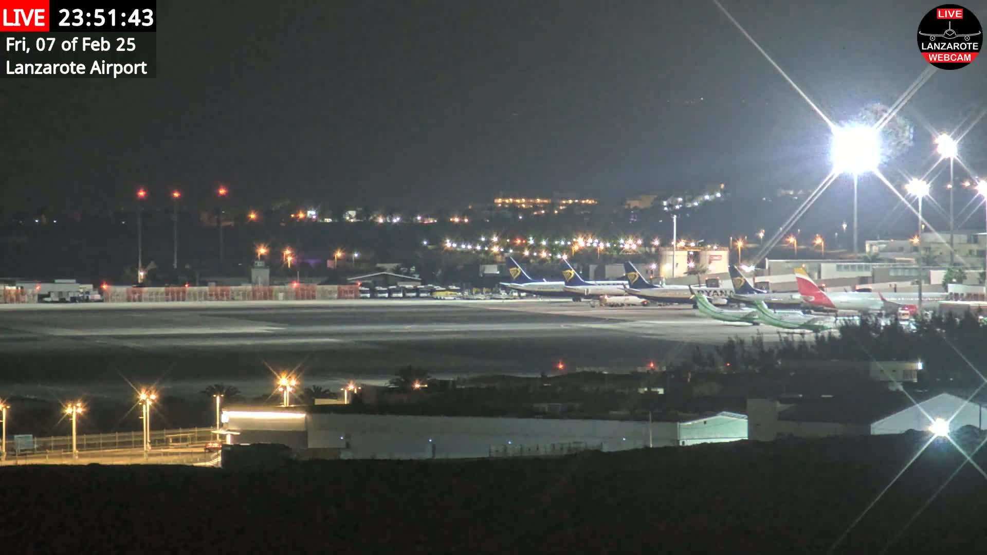 At night, several airplanes are parked on a brightly lit airport tarmac under a clear sky.