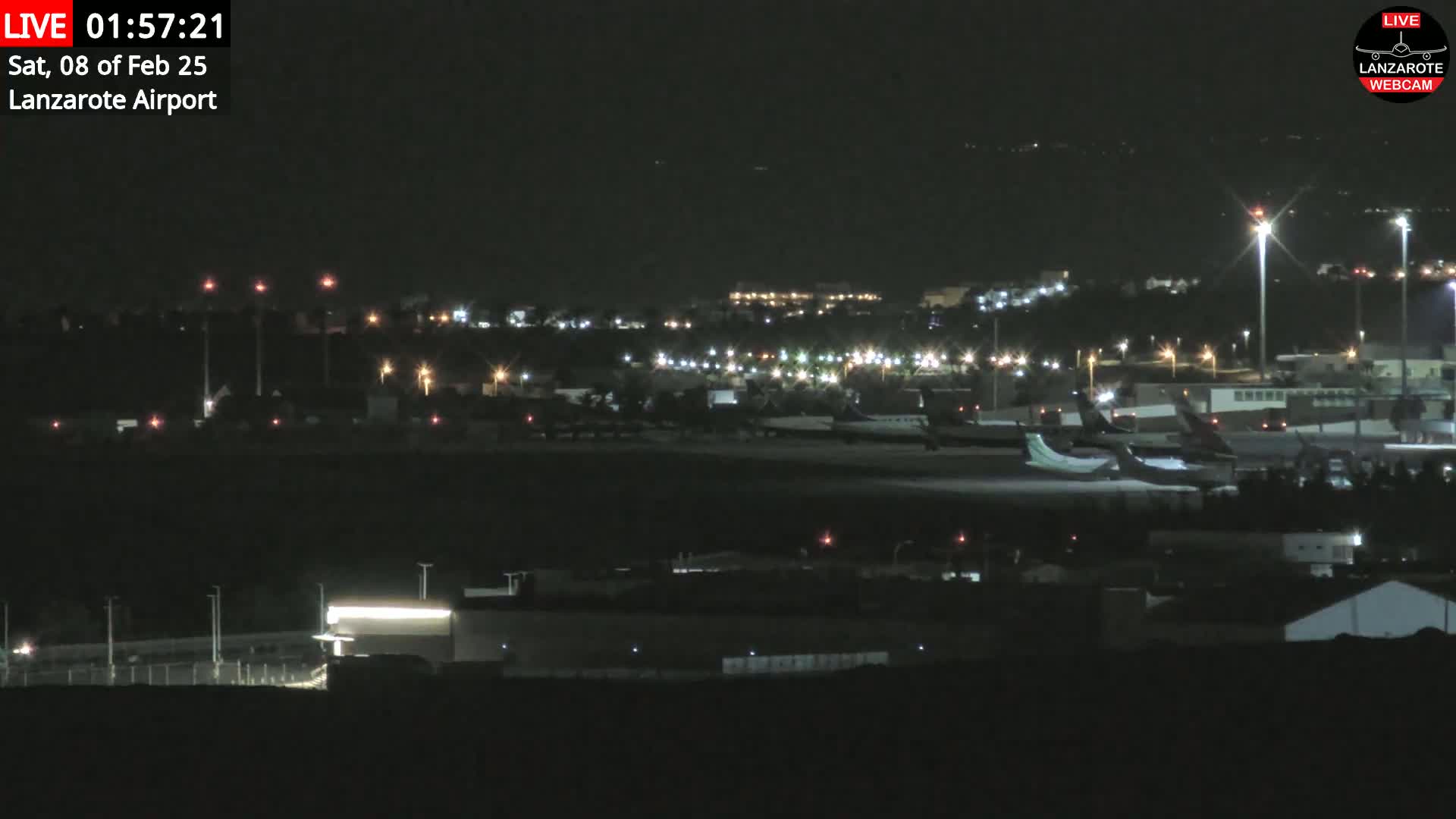 A nighttime view of an airport with several airplanes parked on the tarmac under clear skies.