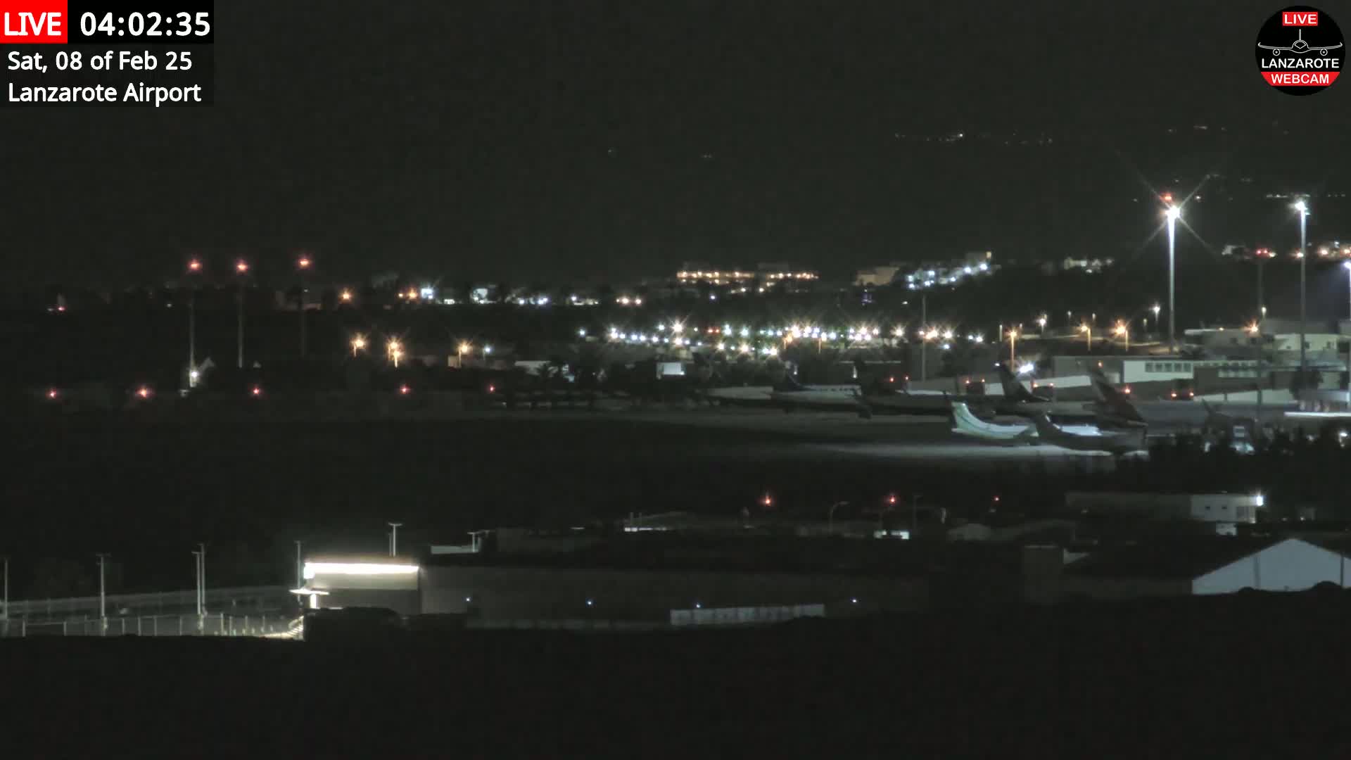 A nighttime view of an airport with several airplanes parked on the tarmac, under a clear, dark sky.