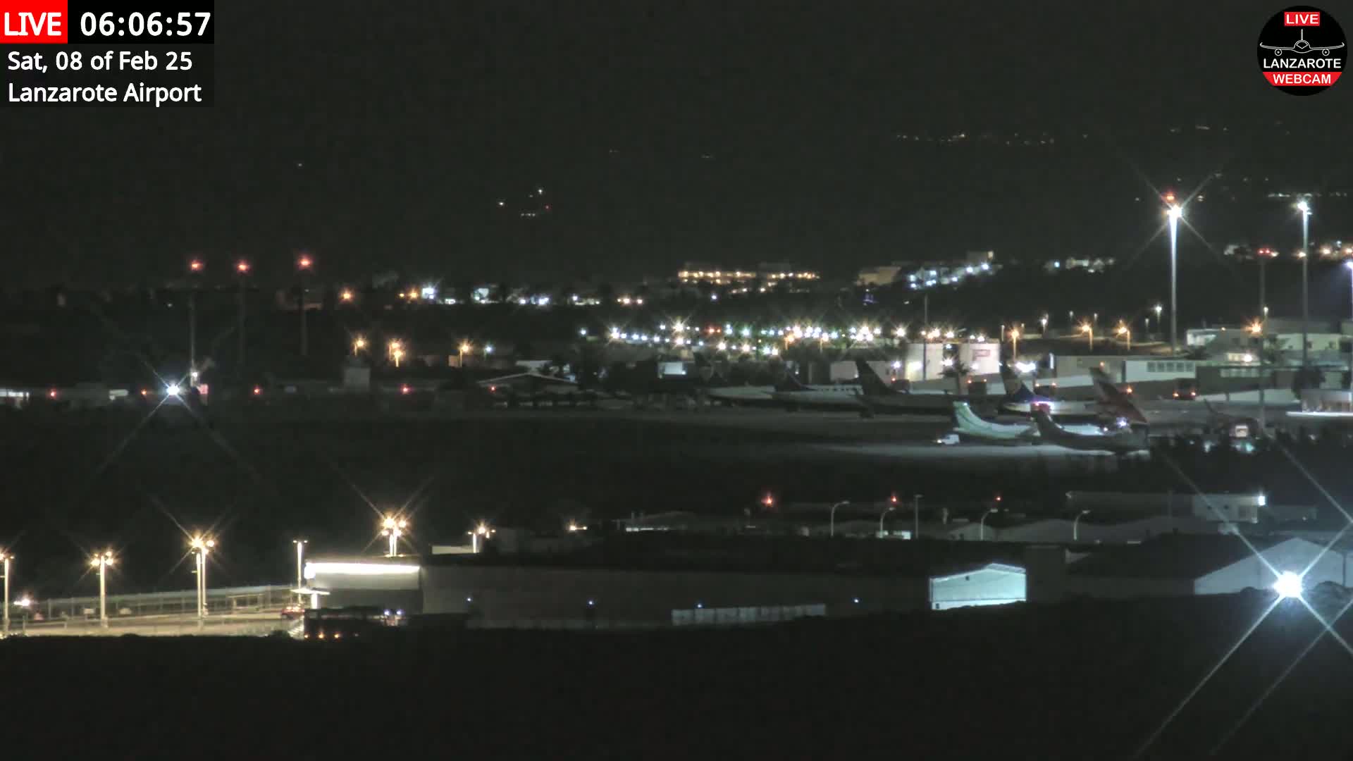 A nighttime view of an airport tarmac with several airplanes parked and illuminated by lights under a clear, dark sky.