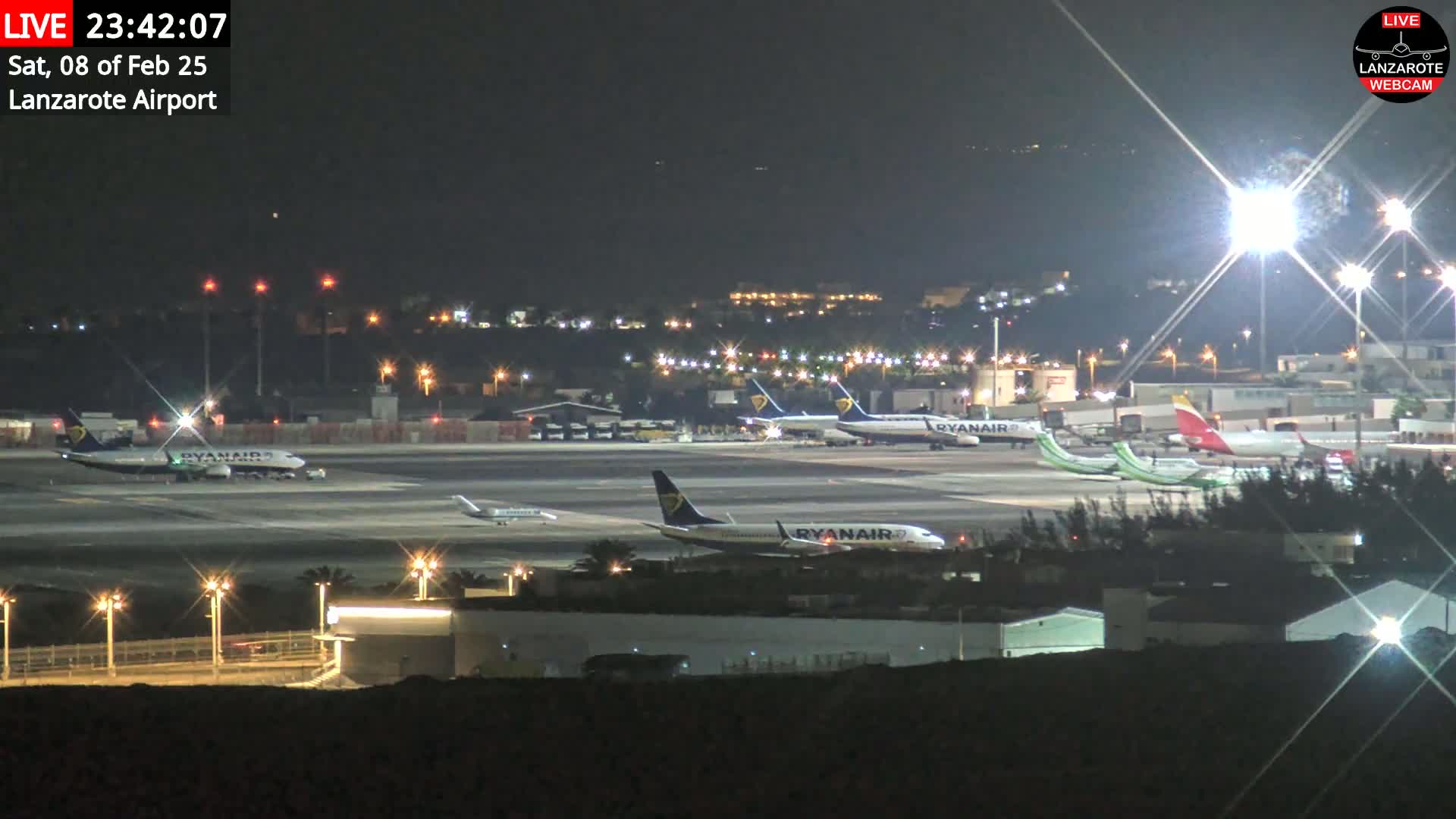 At night, several airplanes are parked on a brightly lit airport tarmac under a clear sky.