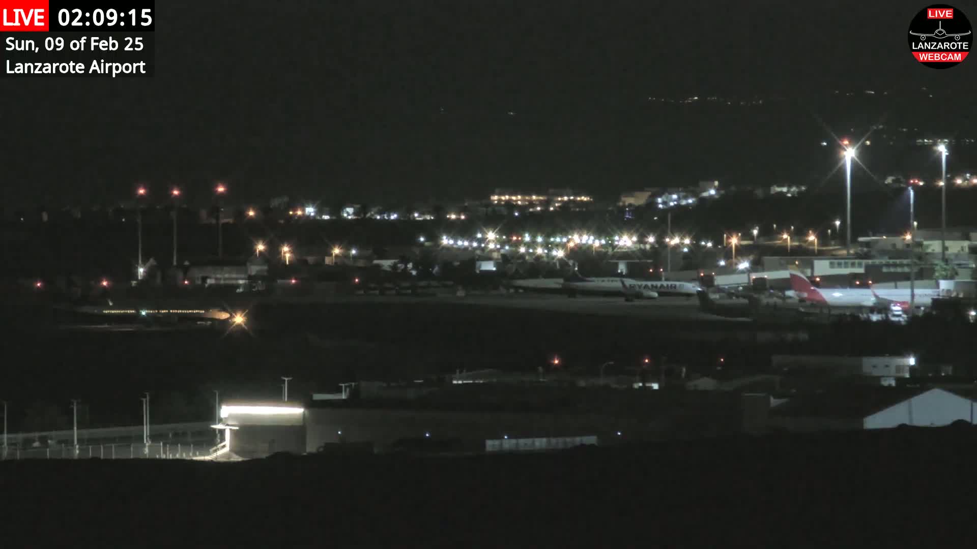 A nighttime view of an airport tarmac with several airplanes and illuminated buildings under a clear, dark sky.
