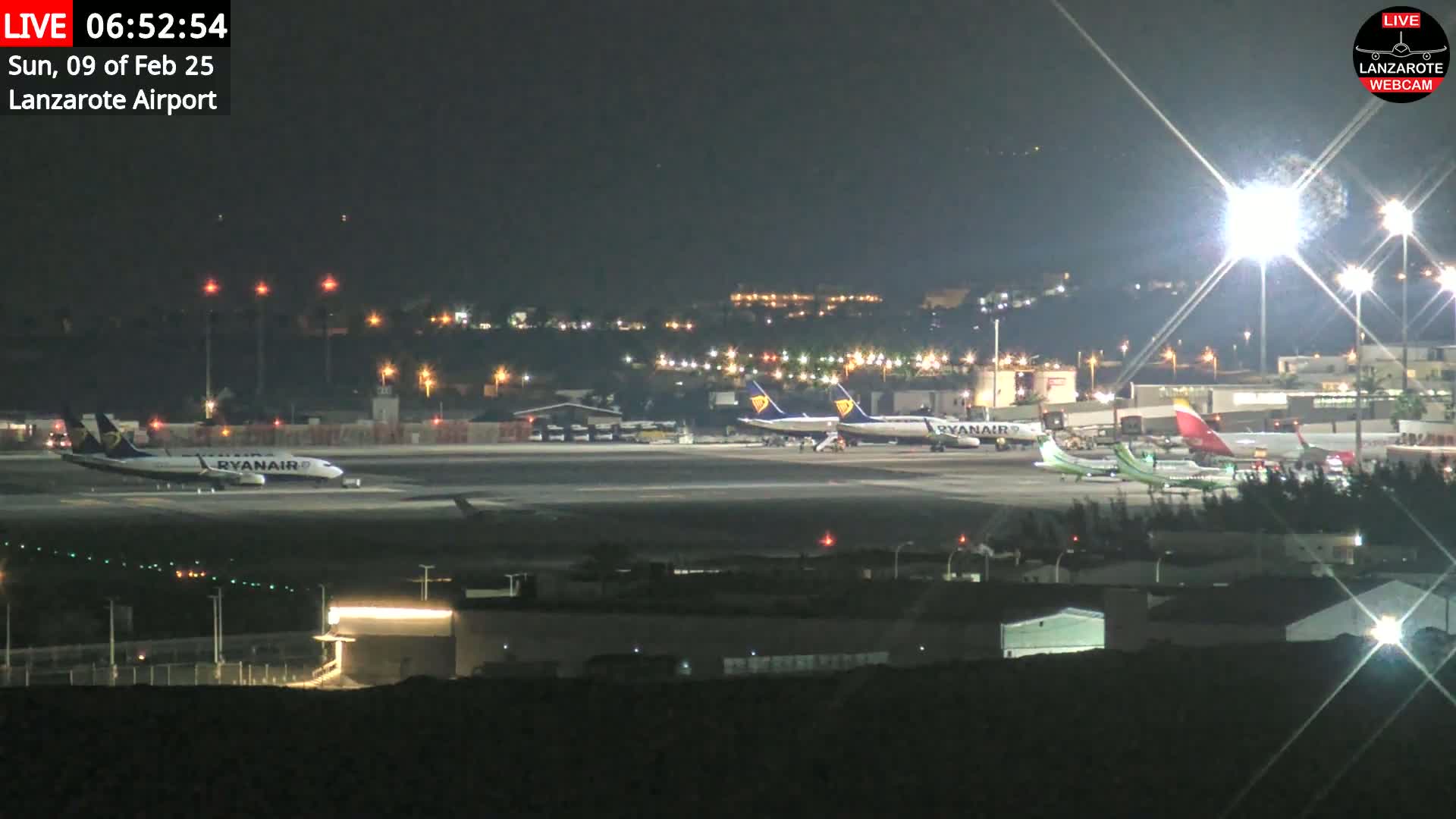 Several airplanes are parked on a brightly lit airport tarmac at night.