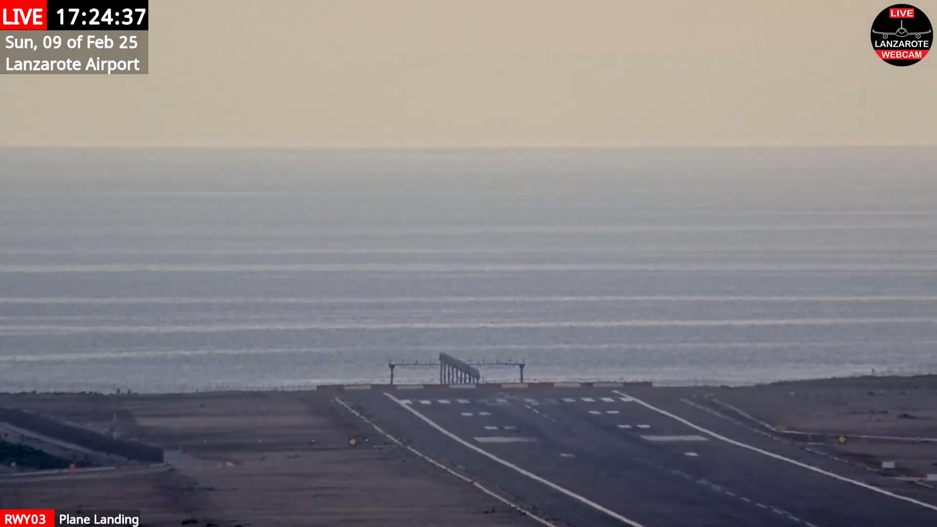 An airport runway extends toward a calm ocean under a hazy sky.
