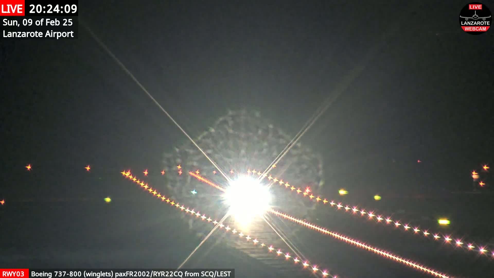 A bright airplane approaches a runway at night, its lights illuminating the ground.
