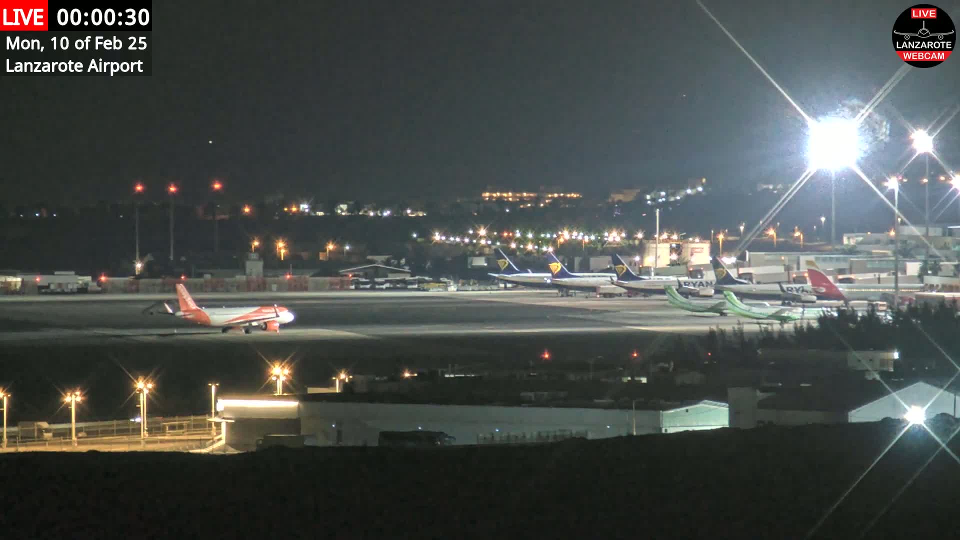 At night, several airplanes are parked on a brightly lit airport tarmac.
