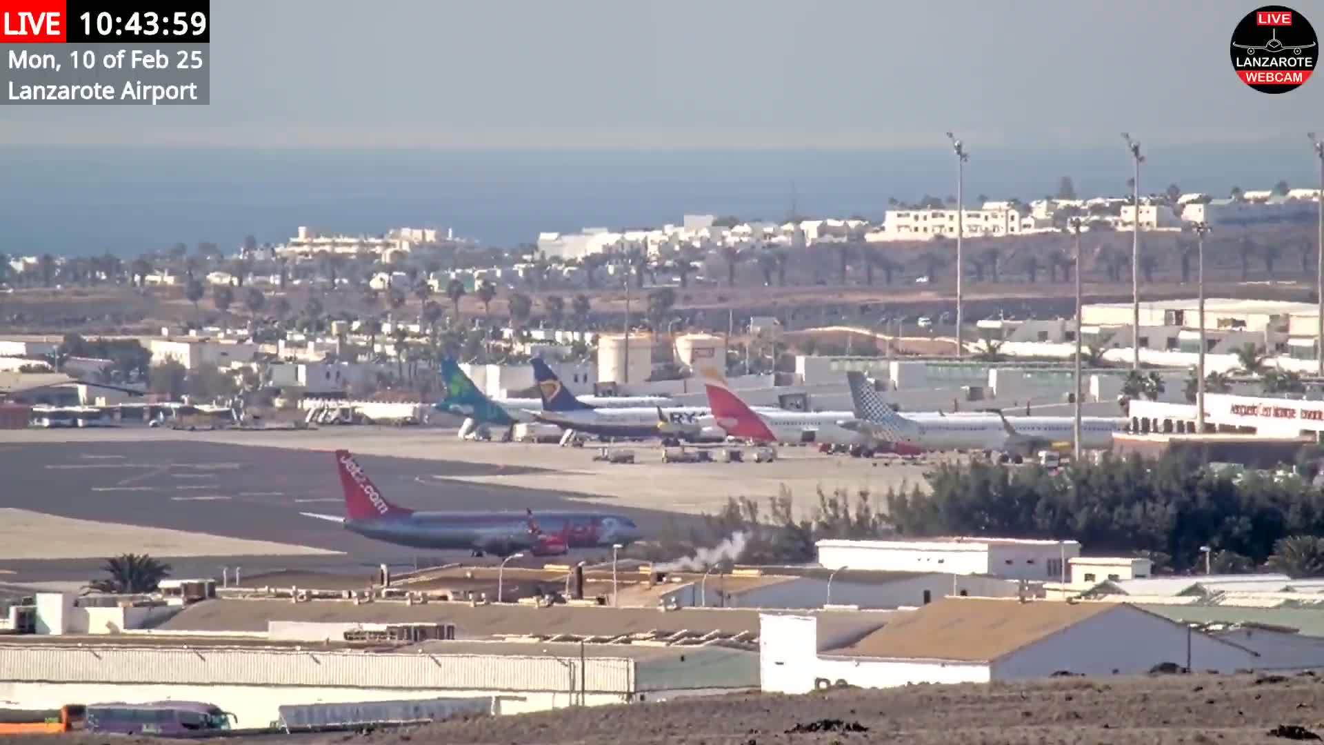 Several airplanes are parked on a tarmac at an airport near a body of water under a clear sky.