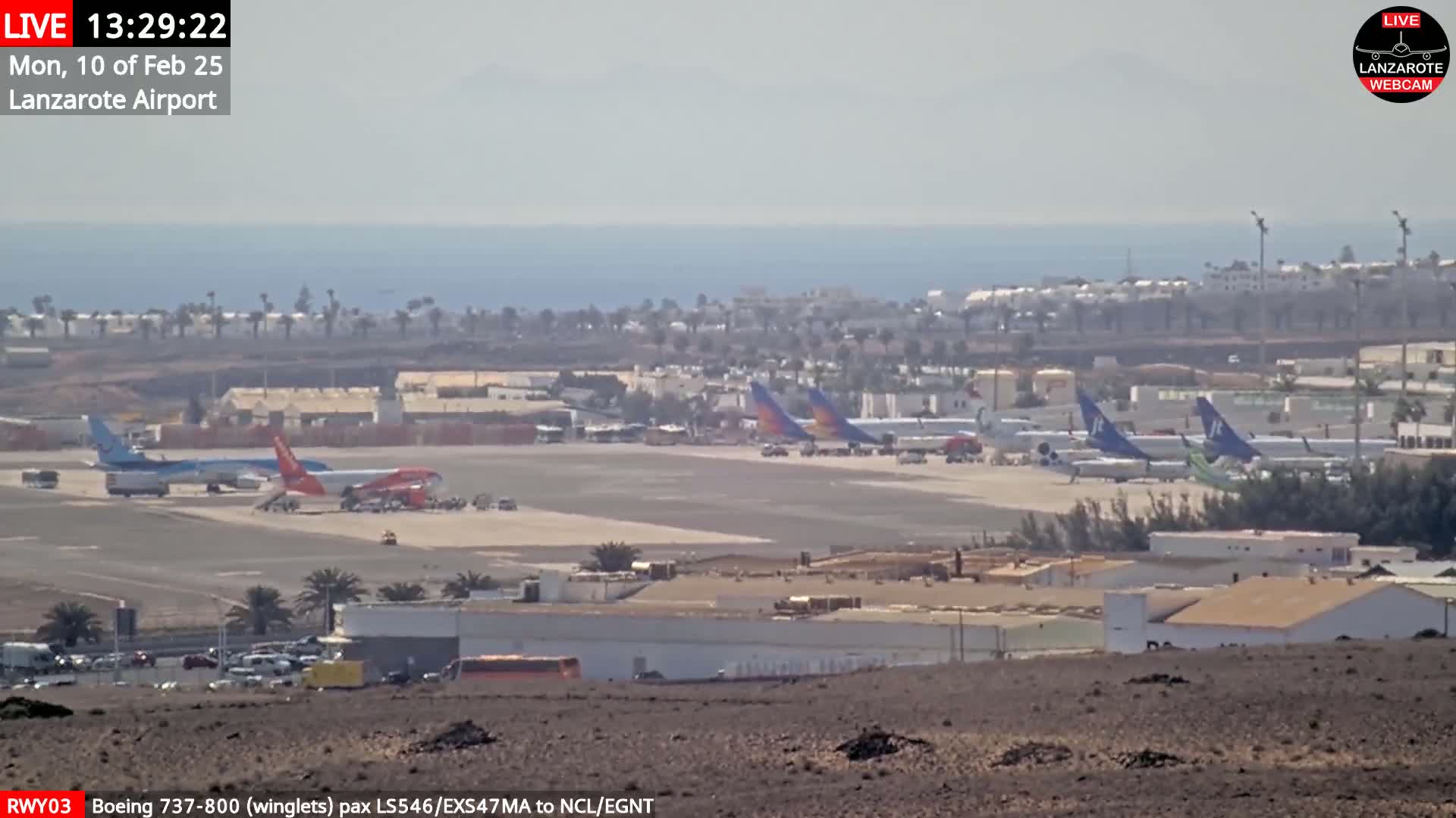 A hazy, sunny day at an airport shows several airplanes parked on the tarmac near a body of water.