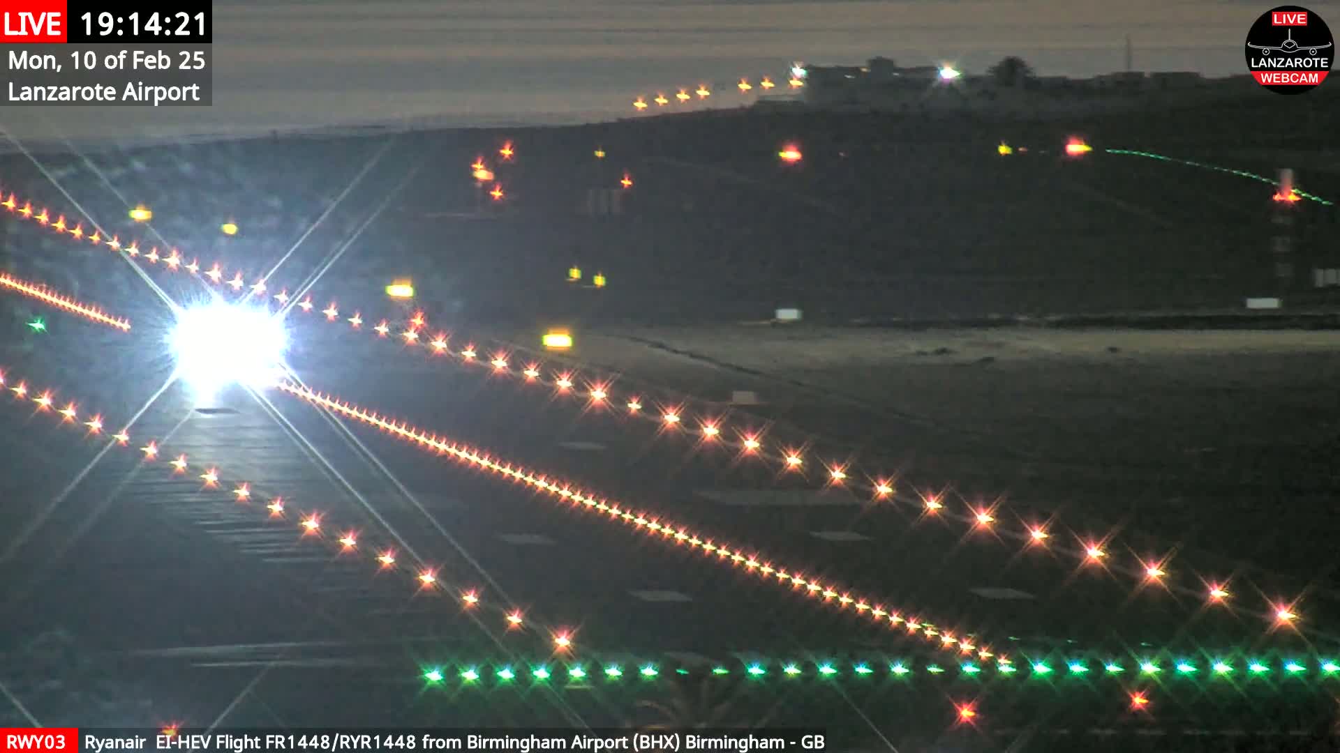 A brightly lit airplane approaches a runway at night under dark, clear skies.