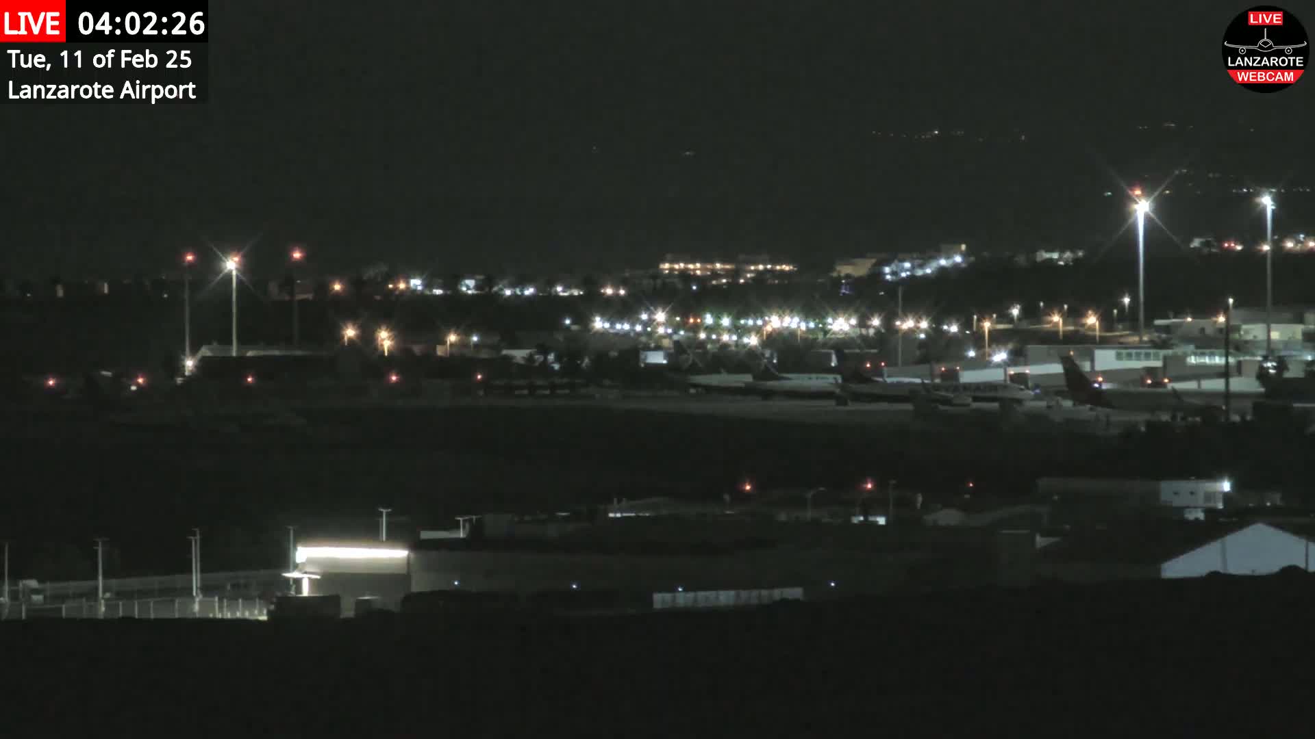 A nighttime view of an airport with numerous lights illuminating planes and buildings on the tarmac under a clear, dark sky.