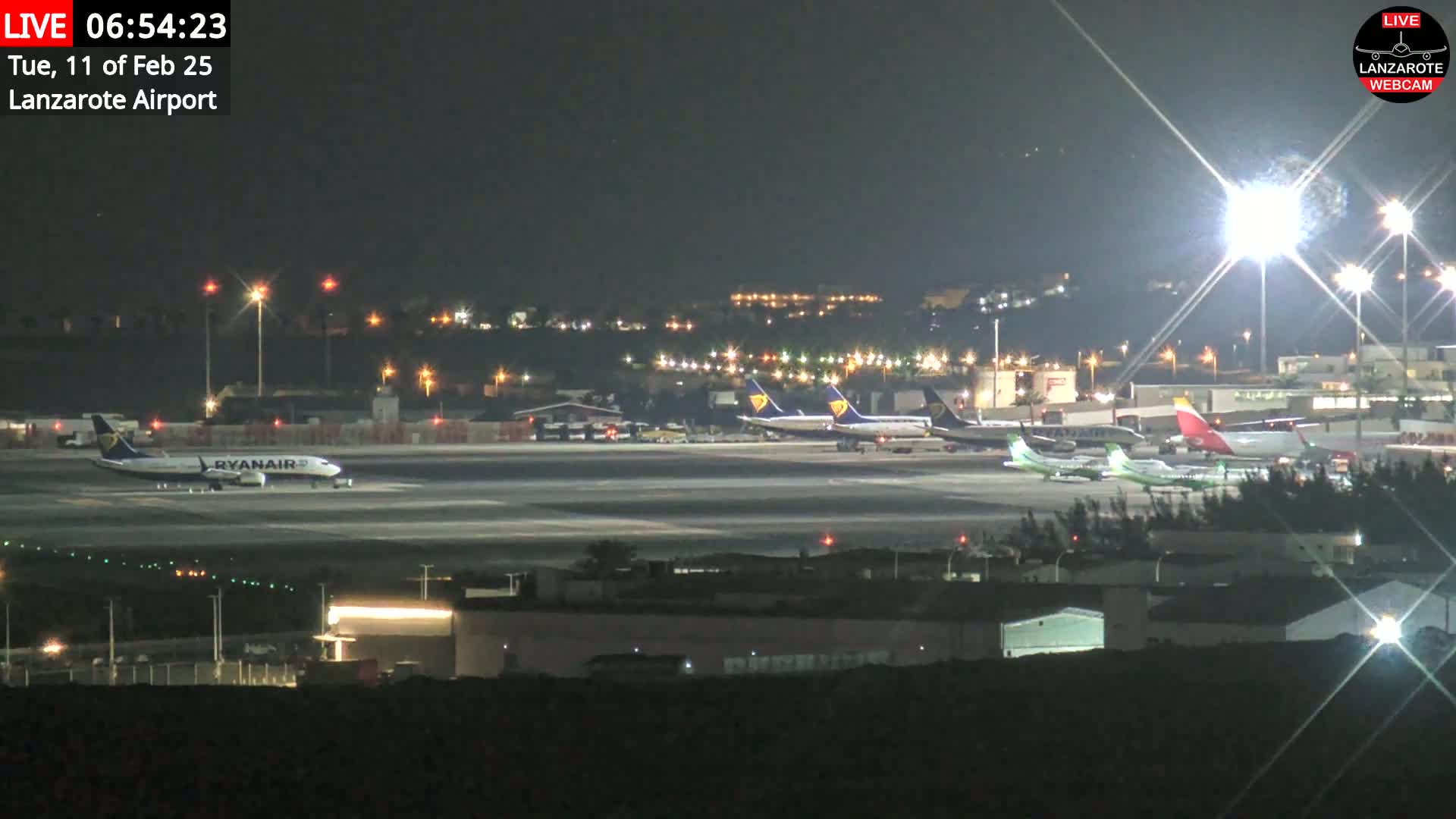 Several airplanes are parked on a brightly lit airport tarmac at night.