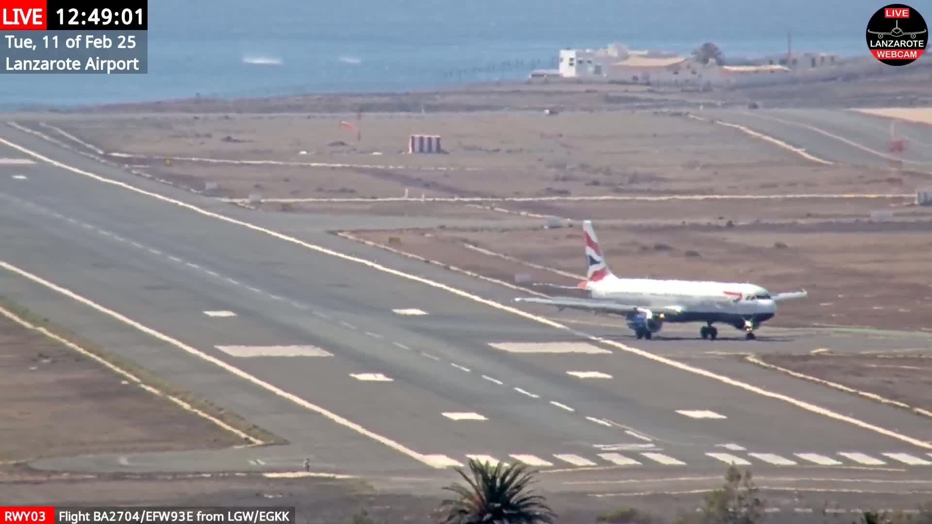 A British Airways airplane taxis on a runway at an airport on a sunny day near a body of water.