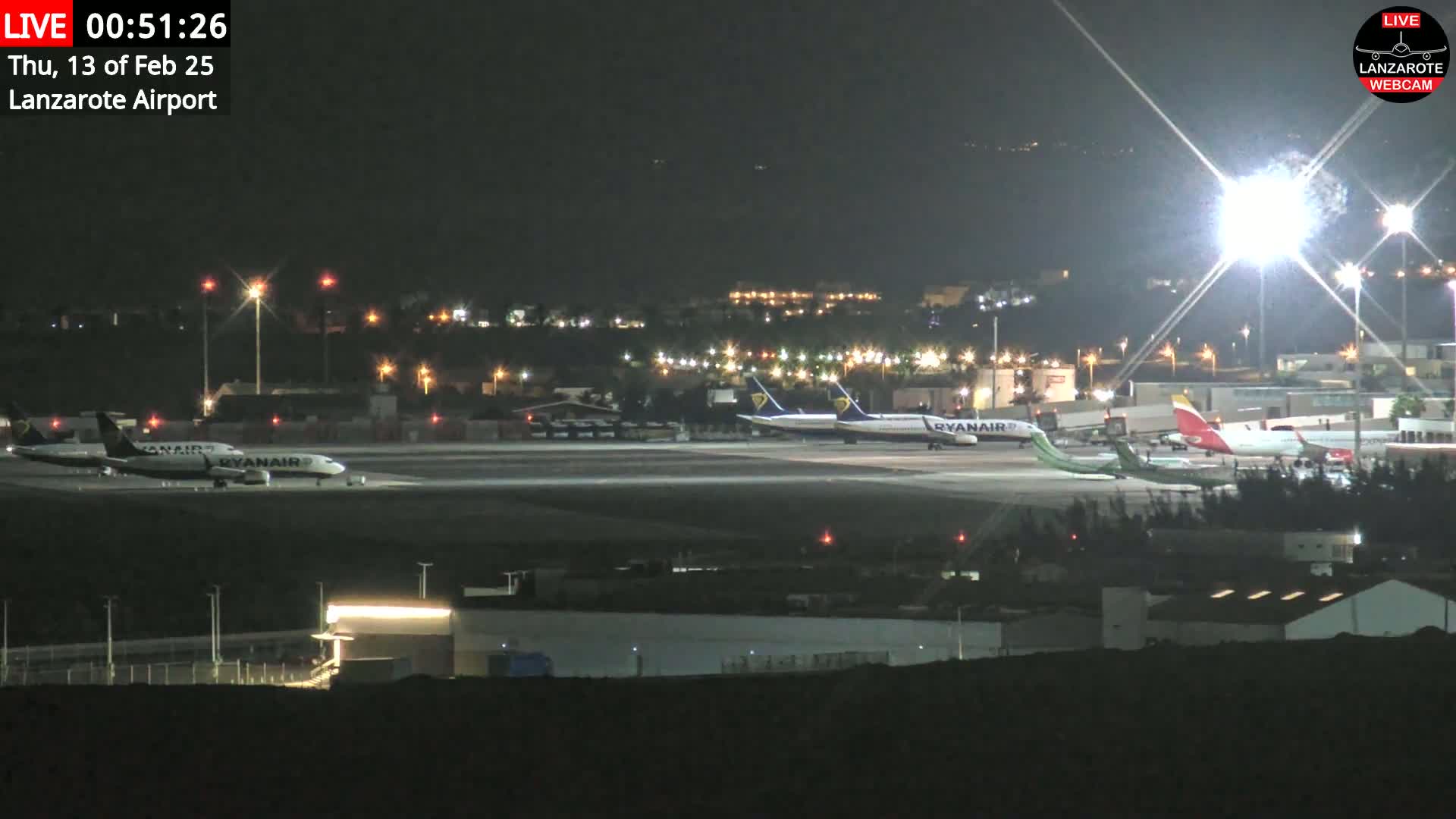 Several airplanes are parked on a brightly lit airport tarmac at night.