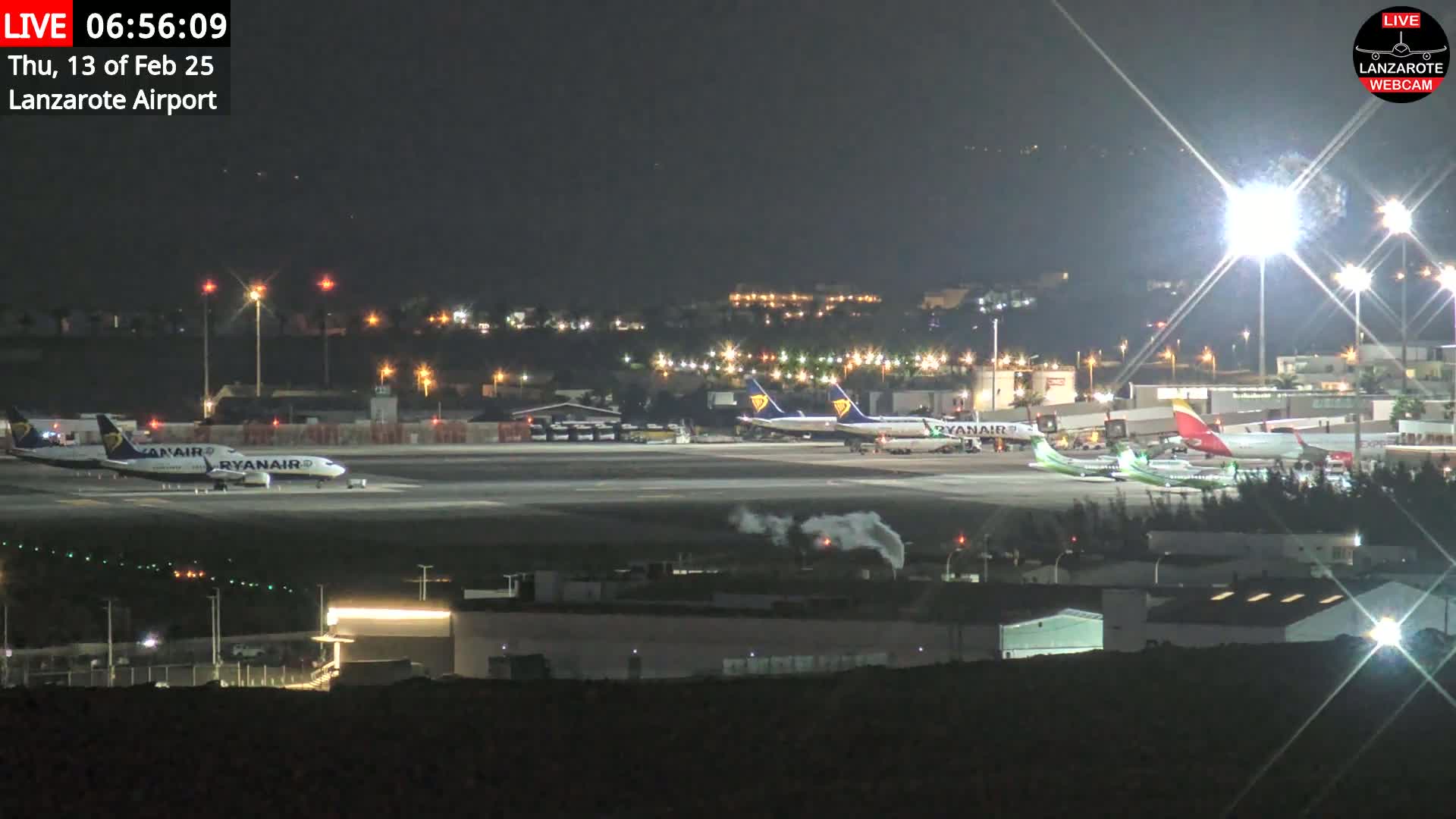 At night, several airplanes are parked on a brightly lit airport tarmac.