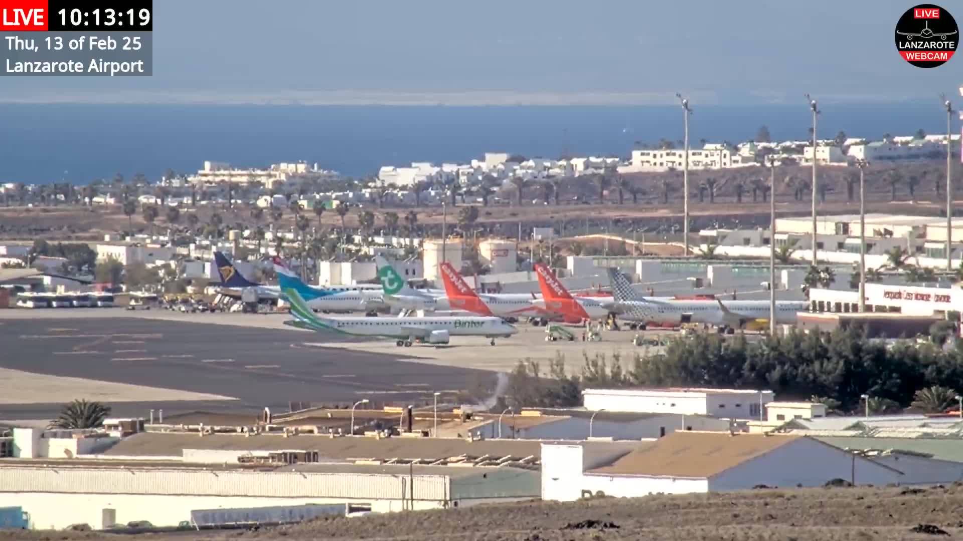 Several airplanes are parked on an airport tarmac near a body of water under a clear sky.