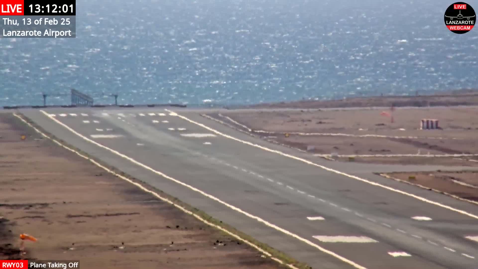 A runway at an airport next to a windy ocean is shown.