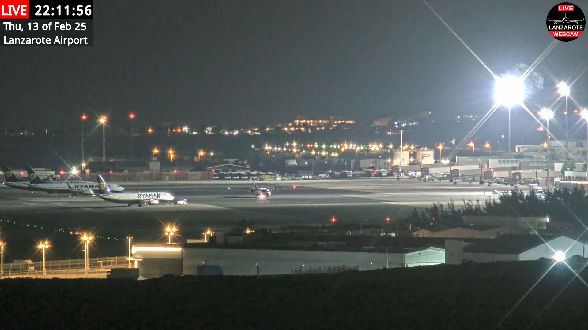 At night, under clear skies, several airplanes are parked on a brightly lit airport tarmac.