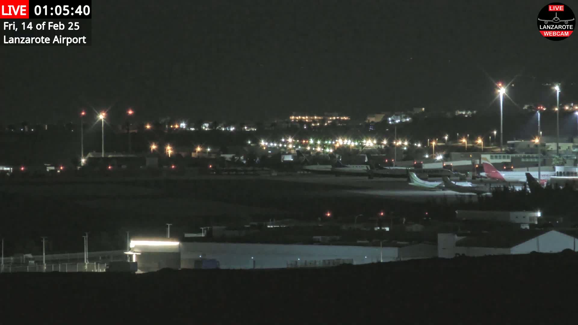 A nighttime view of an airport with several airplanes parked on the tarmac and numerous lights illuminating the surrounding area.