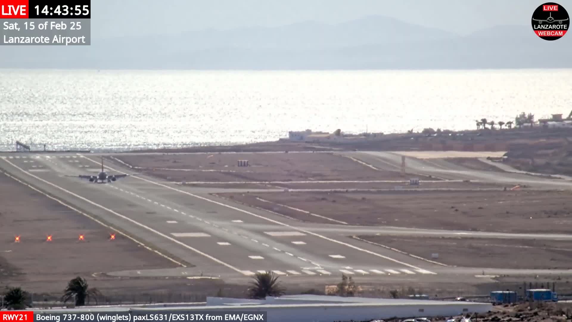 A plane is landing on a runway next to a body of water under a mostly sunny sky.