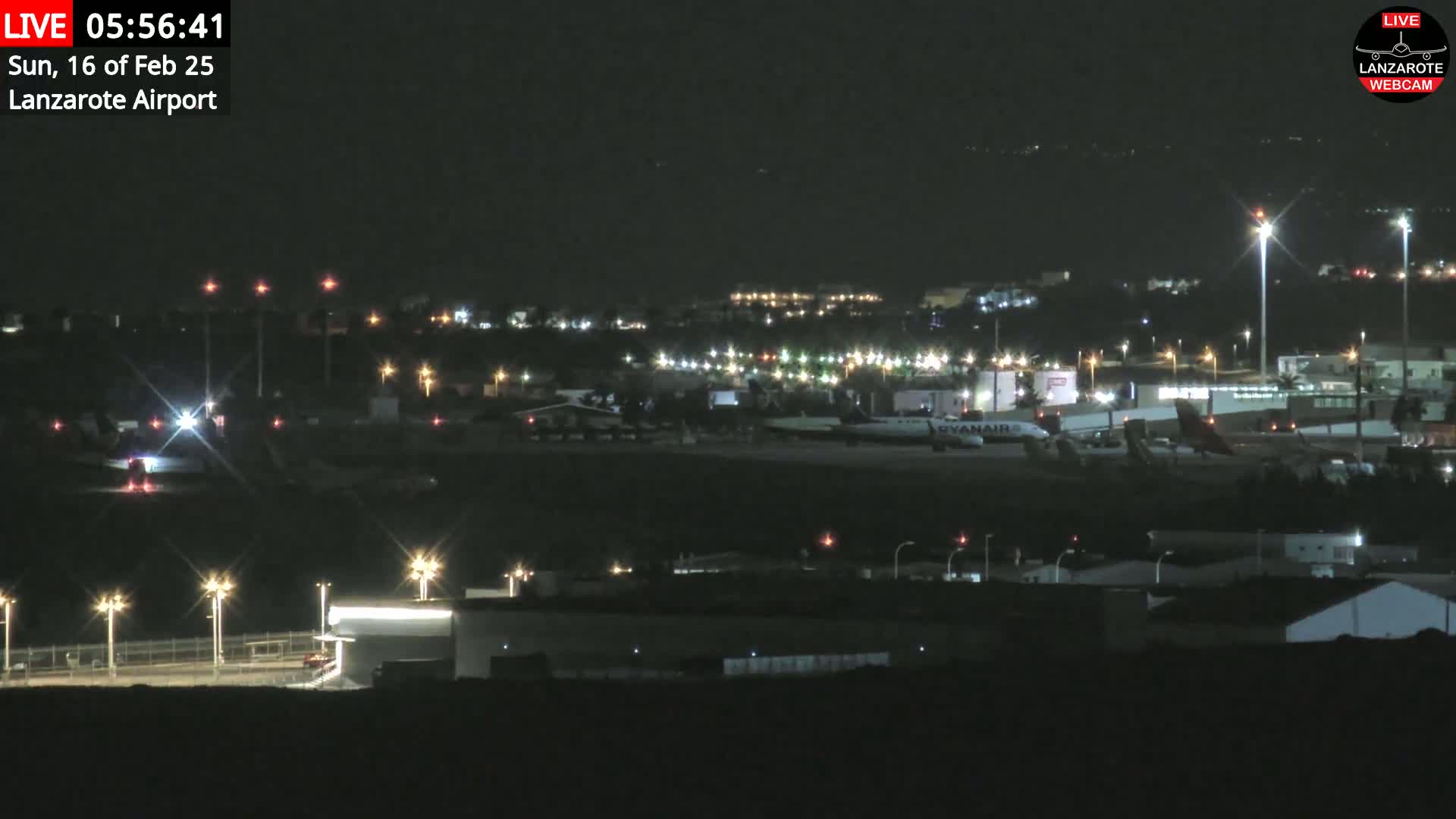 A nighttime view of an airport tarmac with several airplanes and illuminated buildings under a clear, dark sky.