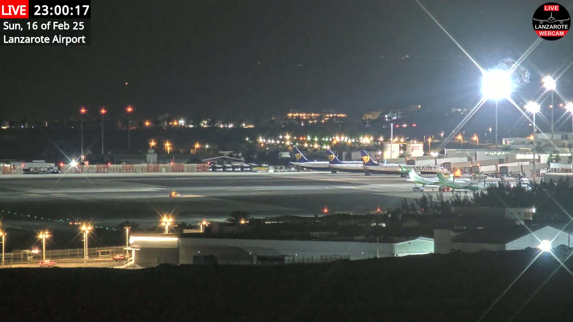 Several airplanes are parked on a brightly lit airport tarmac at night.