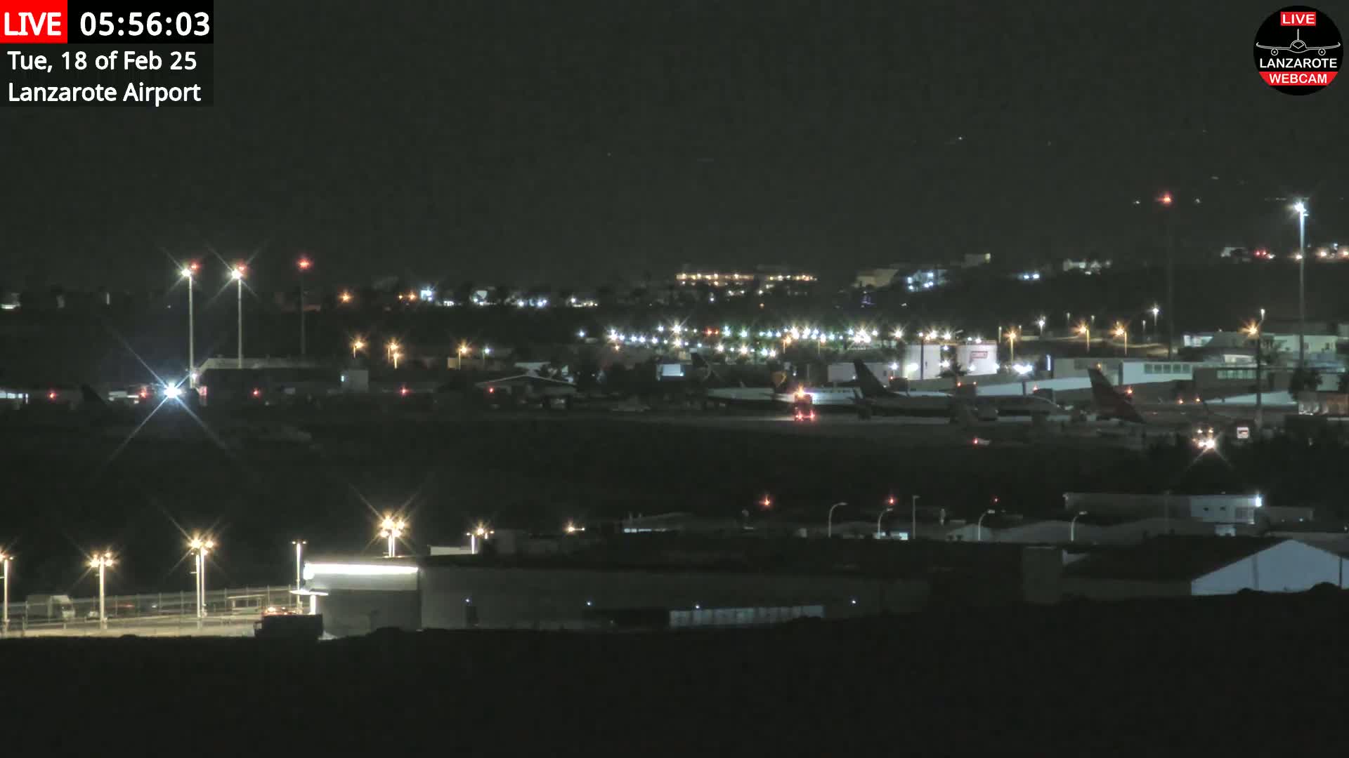 At night, several airplanes are parked on a tarmac surrounded by airport buildings and lights under a clear, dark sky.