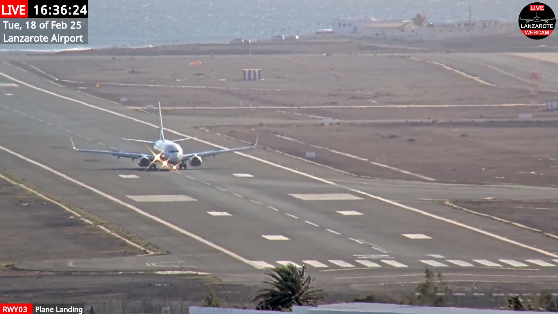 A commercial airplane is landing on a runway at an airport on a partly sunny day.