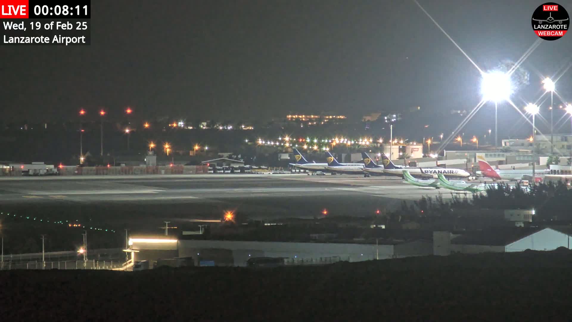 At night, several airplanes are parked on a brightly lit airport tarmac.