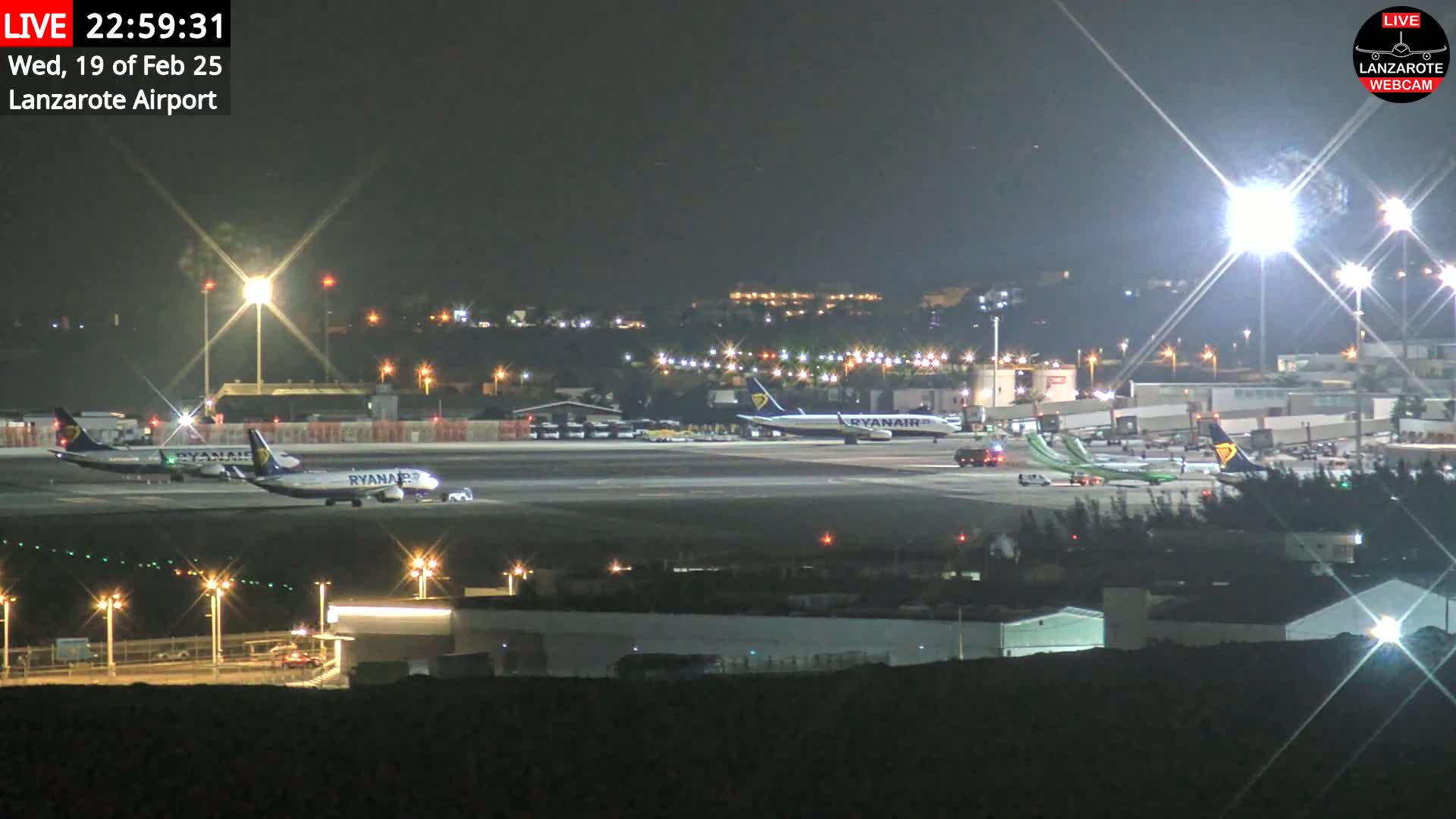 At night, several airplanes are parked on an airport tarmac illuminated by bright lights.