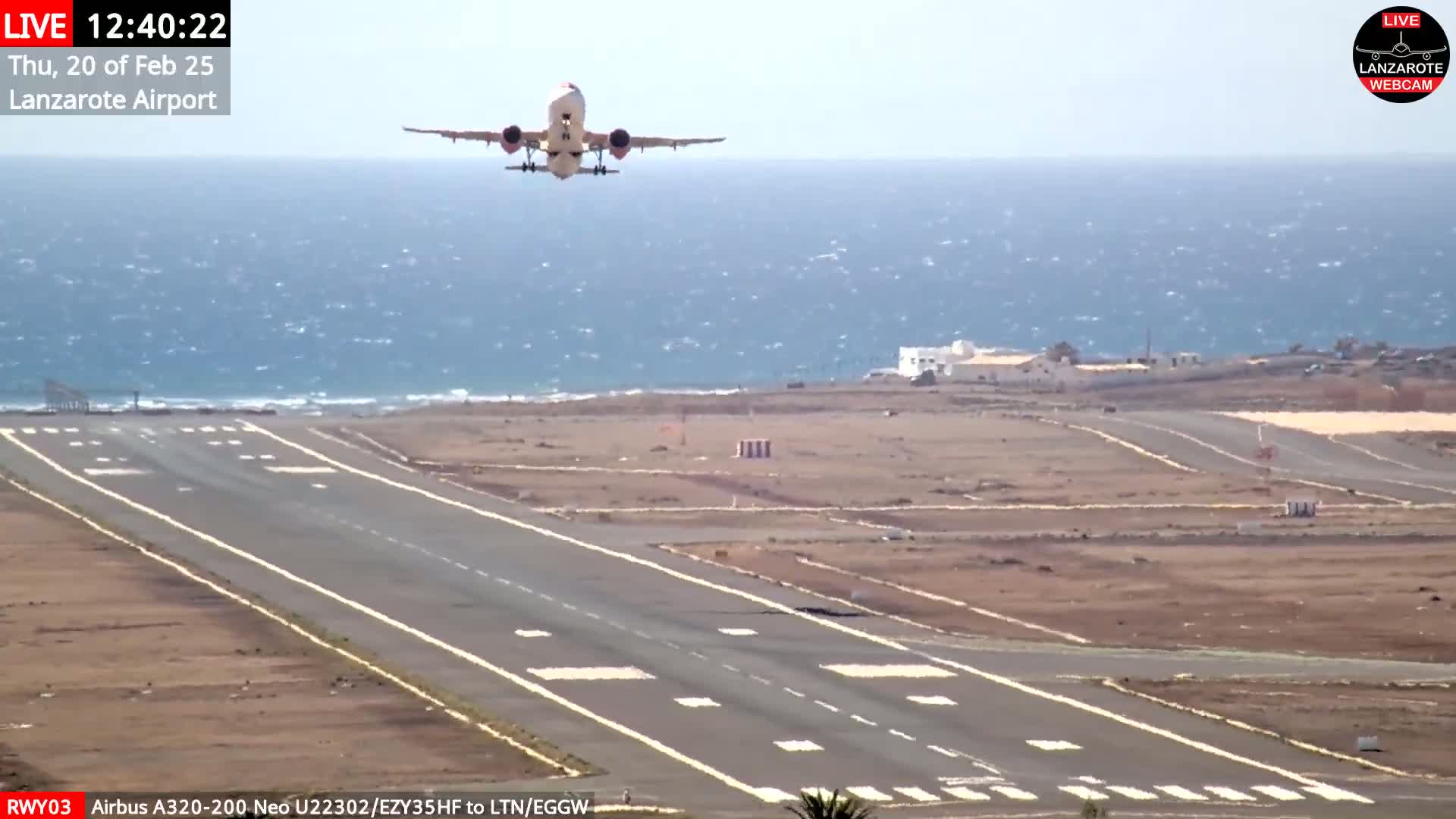 A passenger airplane is taking off from an airport runway next to a body of water under a partly sunny sky with a light breeze.