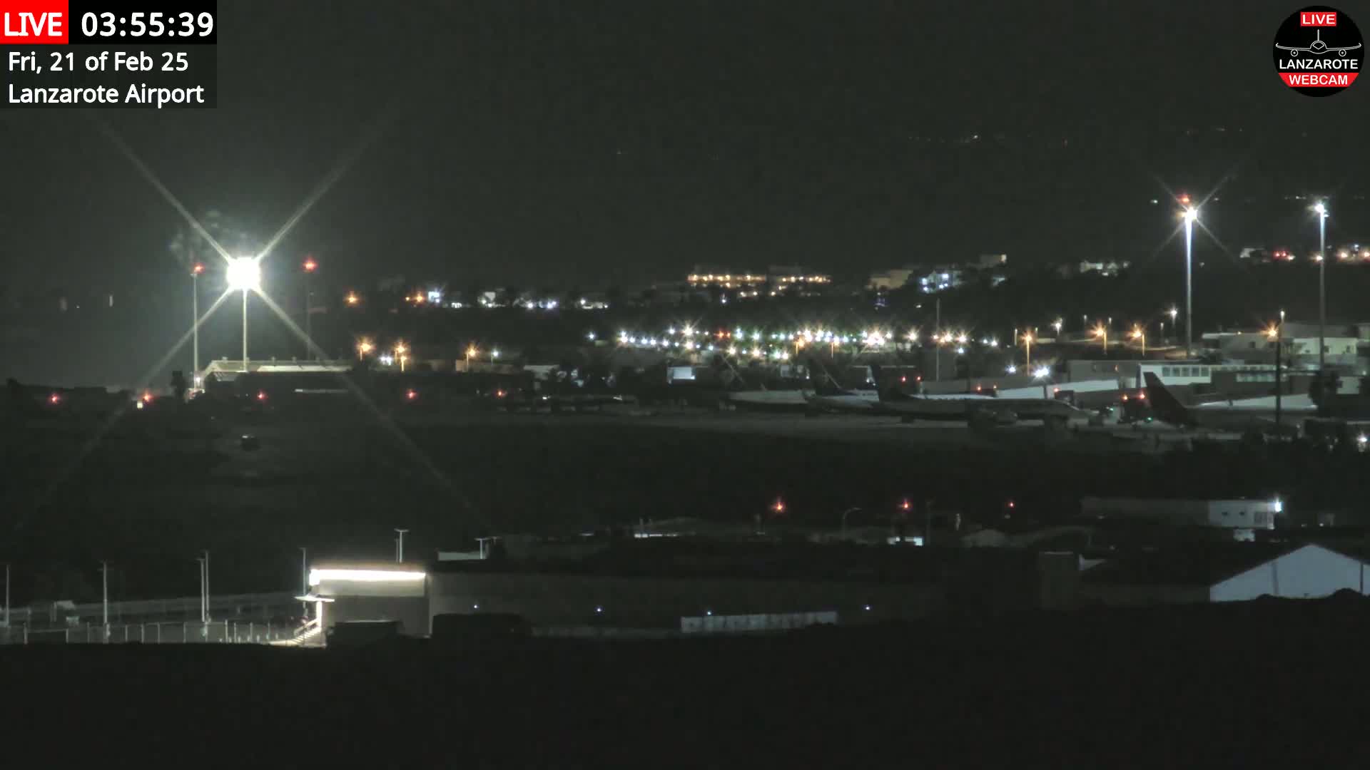 A nighttime view of an airport with several aircraft on the tarmac under clear skies, illuminated by bright lights.