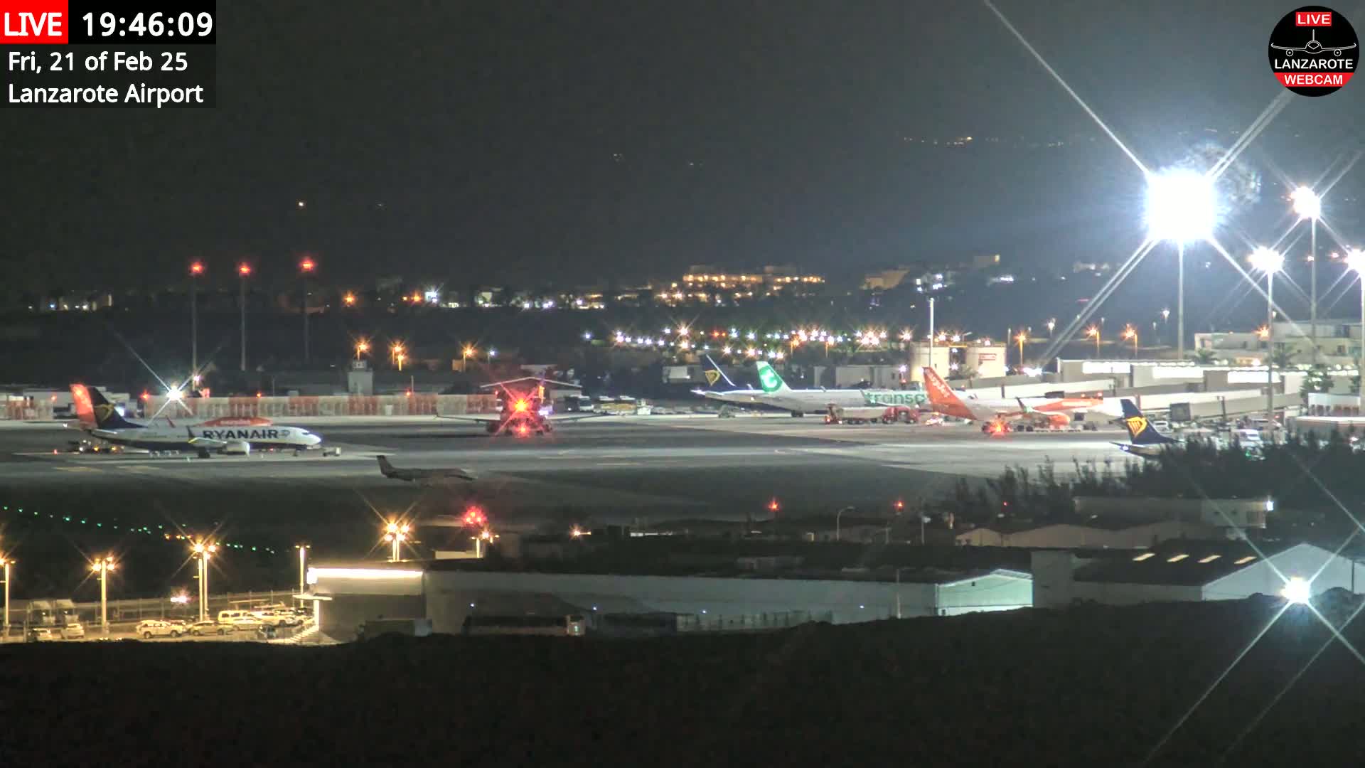 A nighttime view of an airport tarmac with several airplanes parked and illuminated by bright lights.